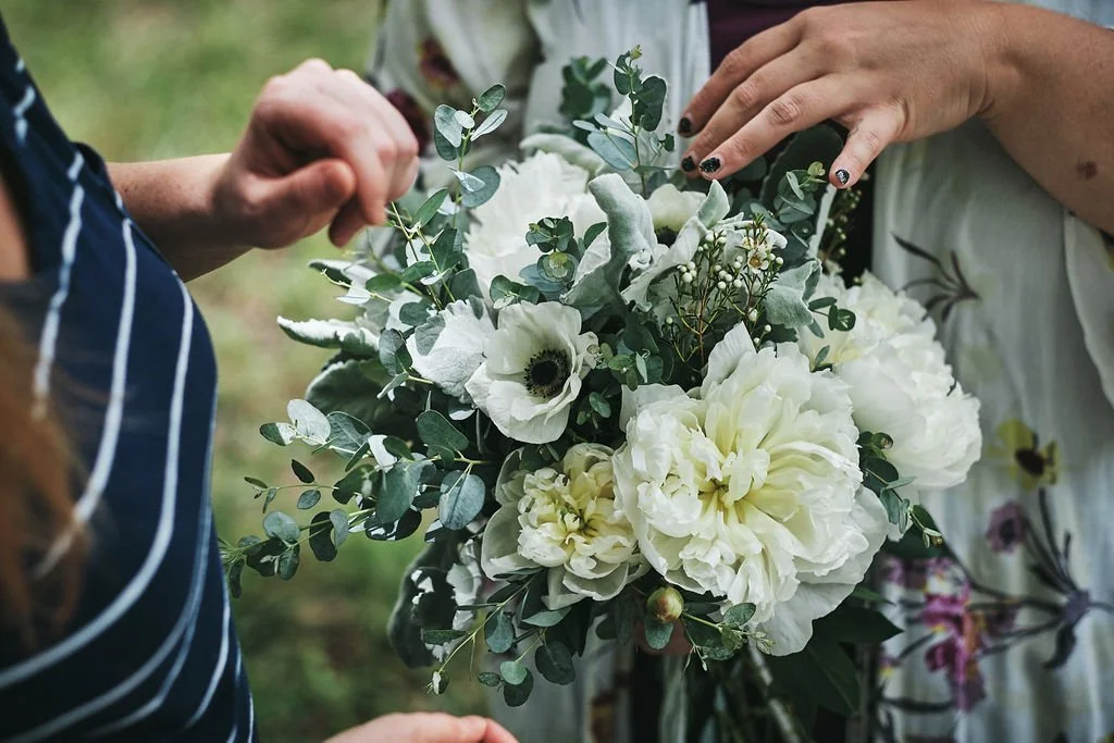 Close-up of two pairs of hands holding a white peony and anemone bridal bouquet with eucalyptus in Blue Ridge Georgia