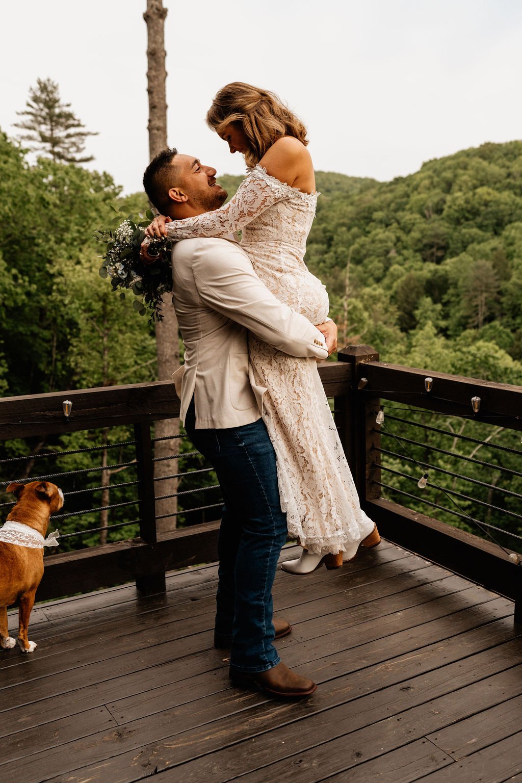 William lifting Erin in a joyful embrace on the cabin deck, both laughing, her blue hydrangea bouquet visible over his shoulder, during their Blue Ridge Georgia elopement