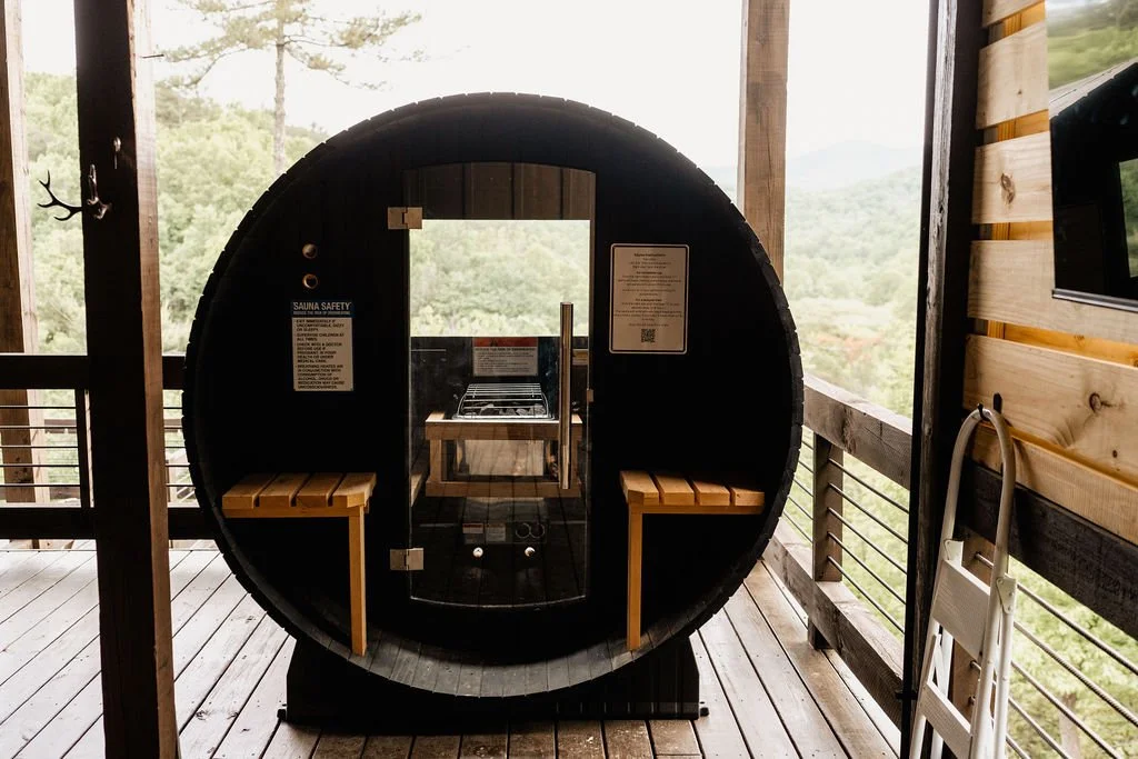 Round barrel sauna on a cabin deck with Appalachian mountain ridgeline visible through the glass door, Blue Ridge Georgia elopement venue detail