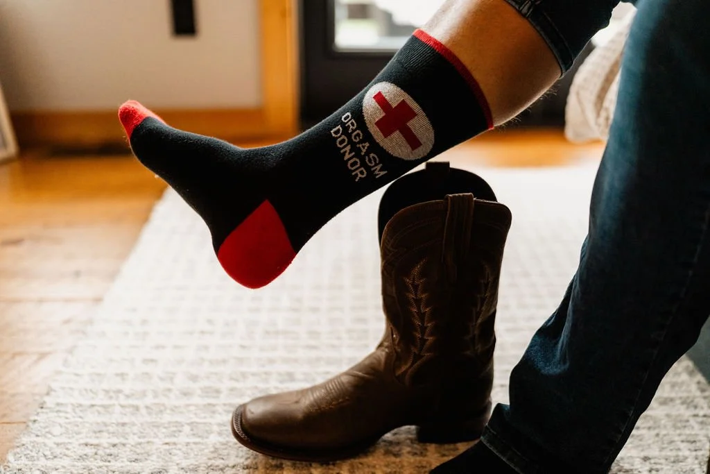 Close-up of William's leg showing humorous organ donor novelty socks with cowboy boots during getting-ready for their Blue Ridge Georgia cabin elopement