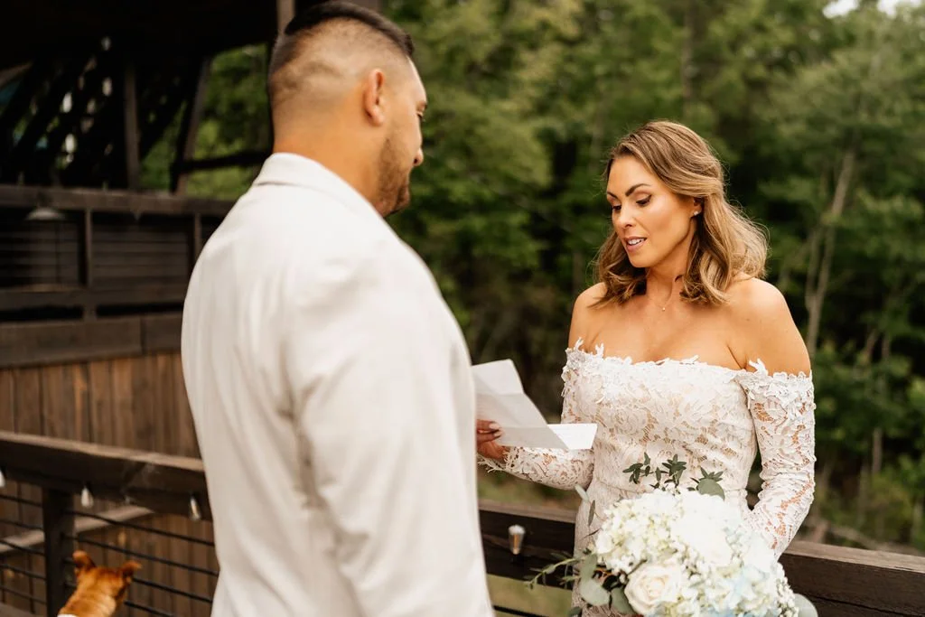 Erin reading her personal vows from a piece of paper on the cabin deck in her lace gown, facing William during their Blue Ridge Georgia elopement ceremony