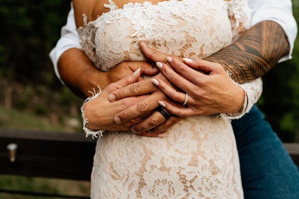 William's tattooed arms wrapped around Erin's waist from behind, both their wedding rings visible, during their Blue Ridge Georgia cabin elopement
