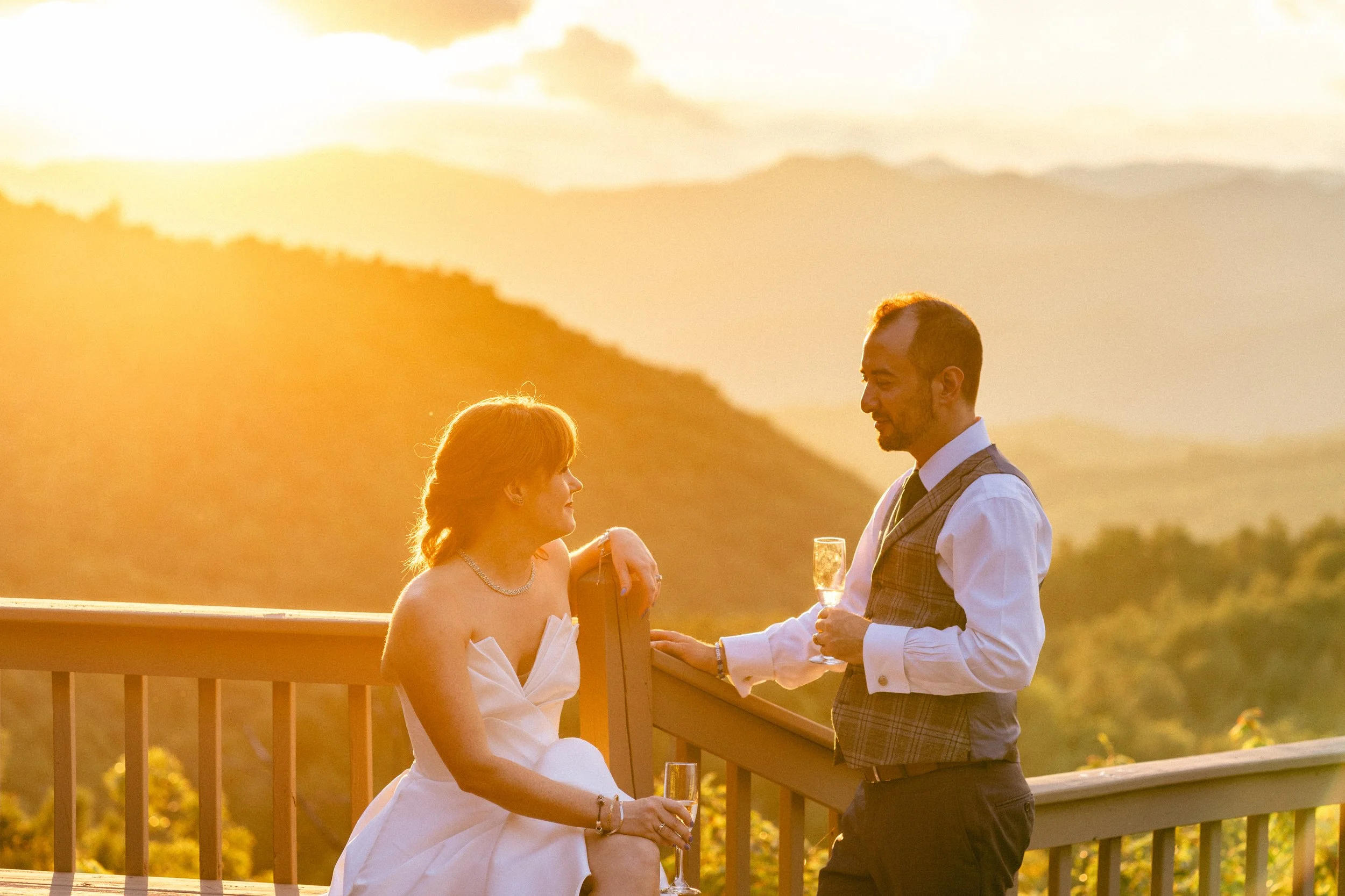 Couple toasting champagne on a mountain deck during golden hour at their Blue Ridge wedding