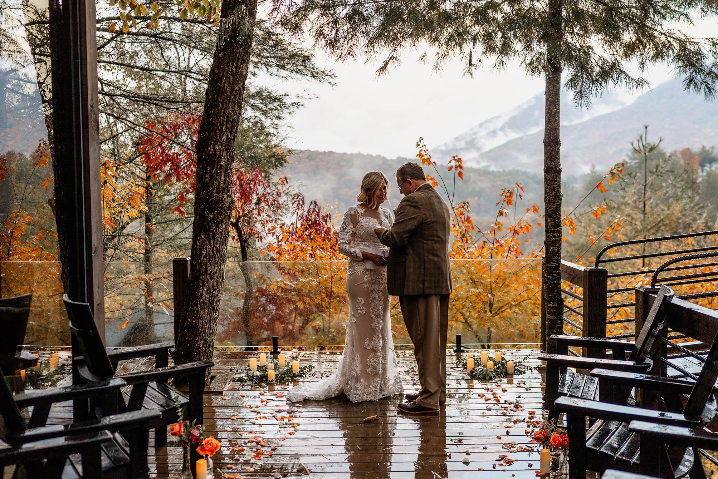Couple exchanging vows on a rainy deck with fall foliage and snow mountain backdrop at their Appalachian wedding
