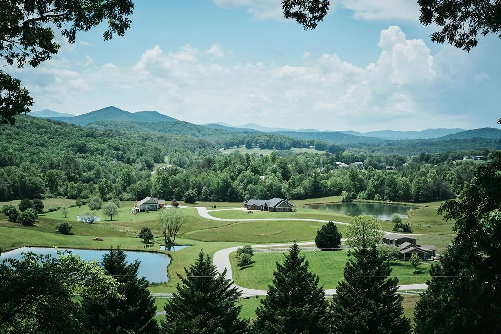 Wide landscape view of a green valley with ponds and farmhouse buildings surrounded by Blue Ridge Georgia mountain ridgelines