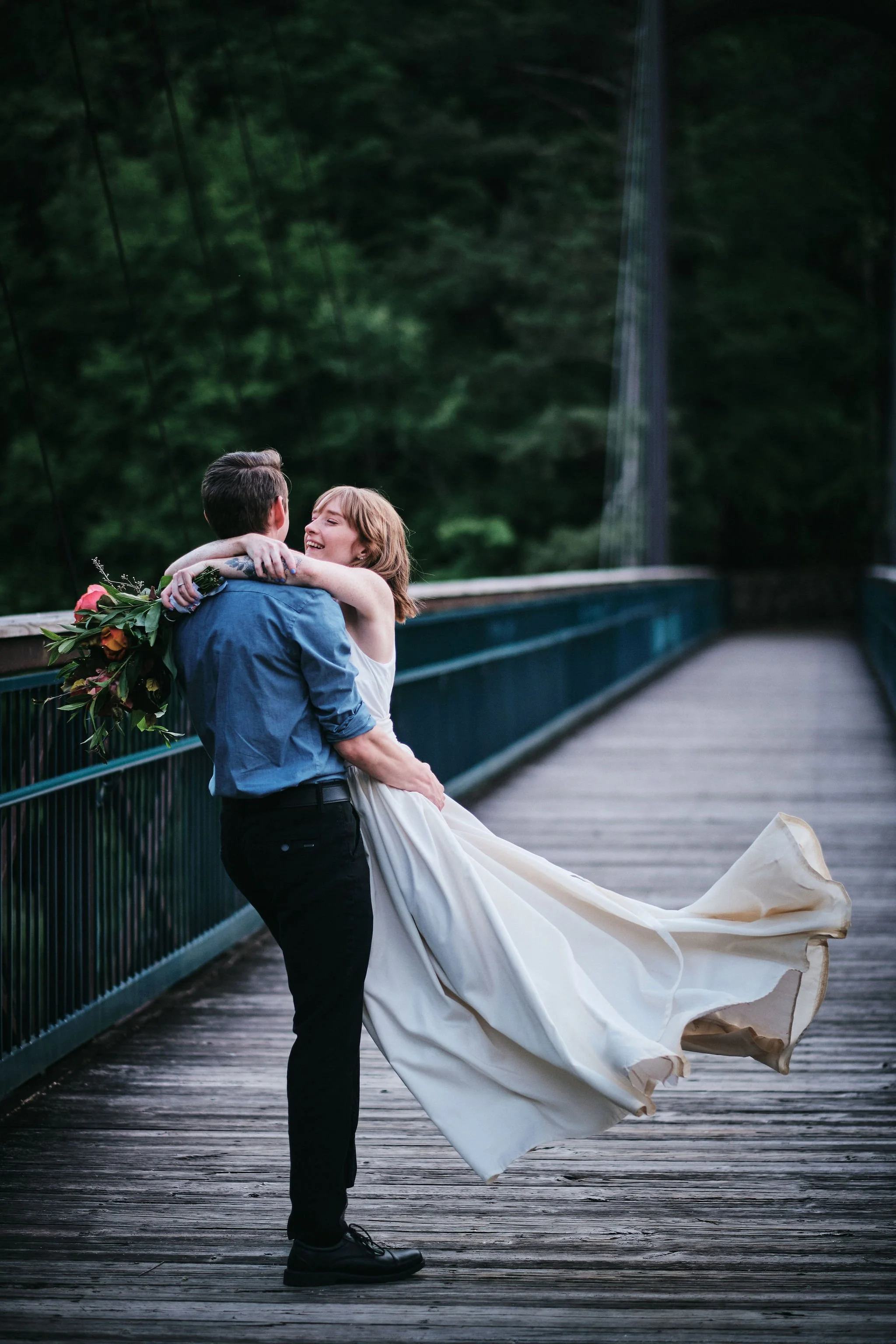Keene dipping Margo in a romantic embrace on a Blue Ridge mountain bridge, her white elopement dress flowing, North Georgia intimate elopement photography