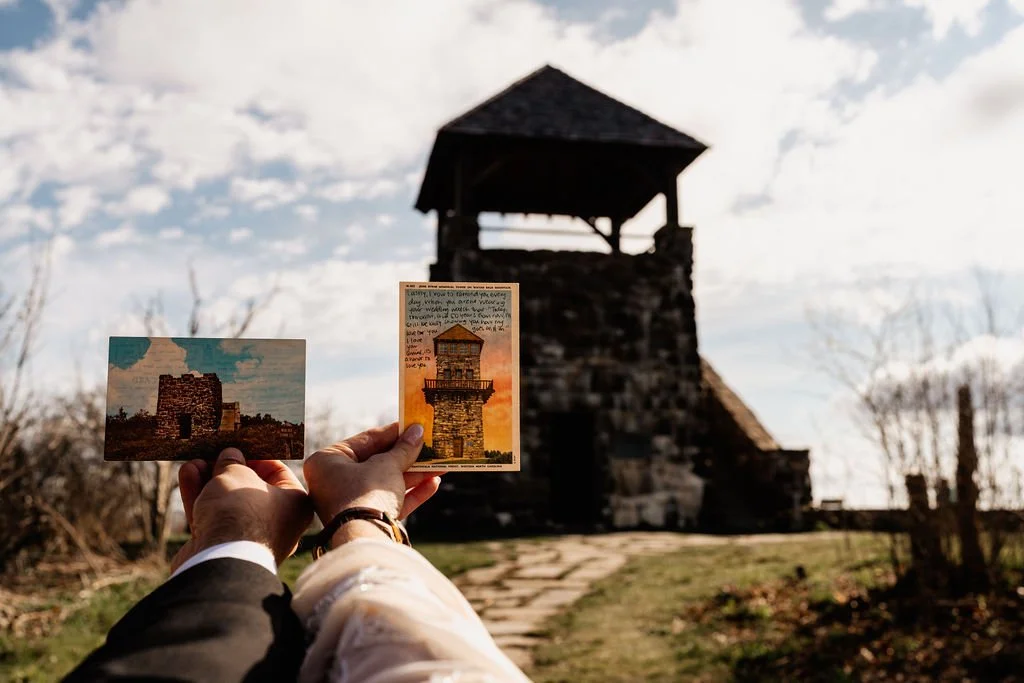 Couple holding vintage Wayah Bald postcards with the historic stone fire tower in the background during their intimate mountain elopement in the Nantahala National Forest, North Carolina