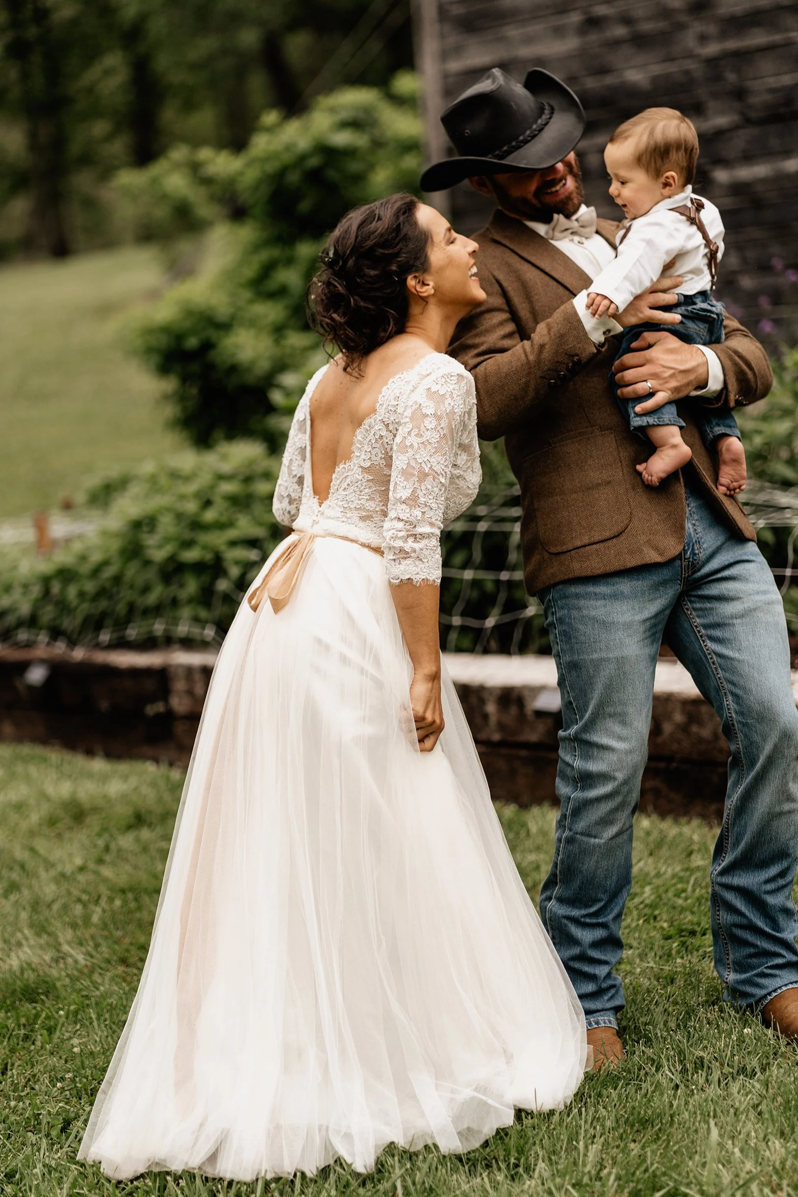 Nick and Anna with husband carrying baby outdoors in a lace gown during their Appalachian wedding
