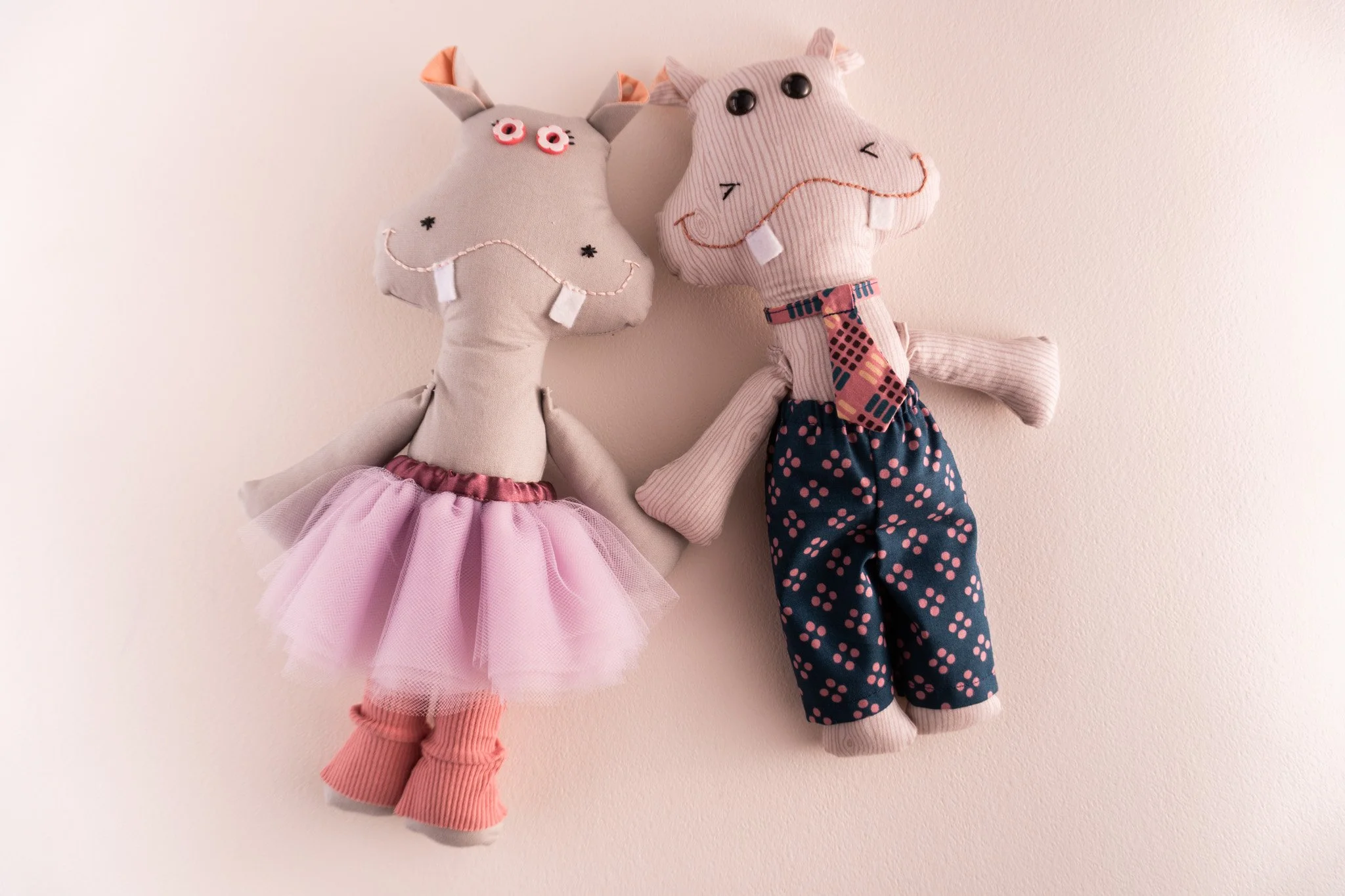 Two hippo dolls, one in a tutu and one in pants and a neck tie.