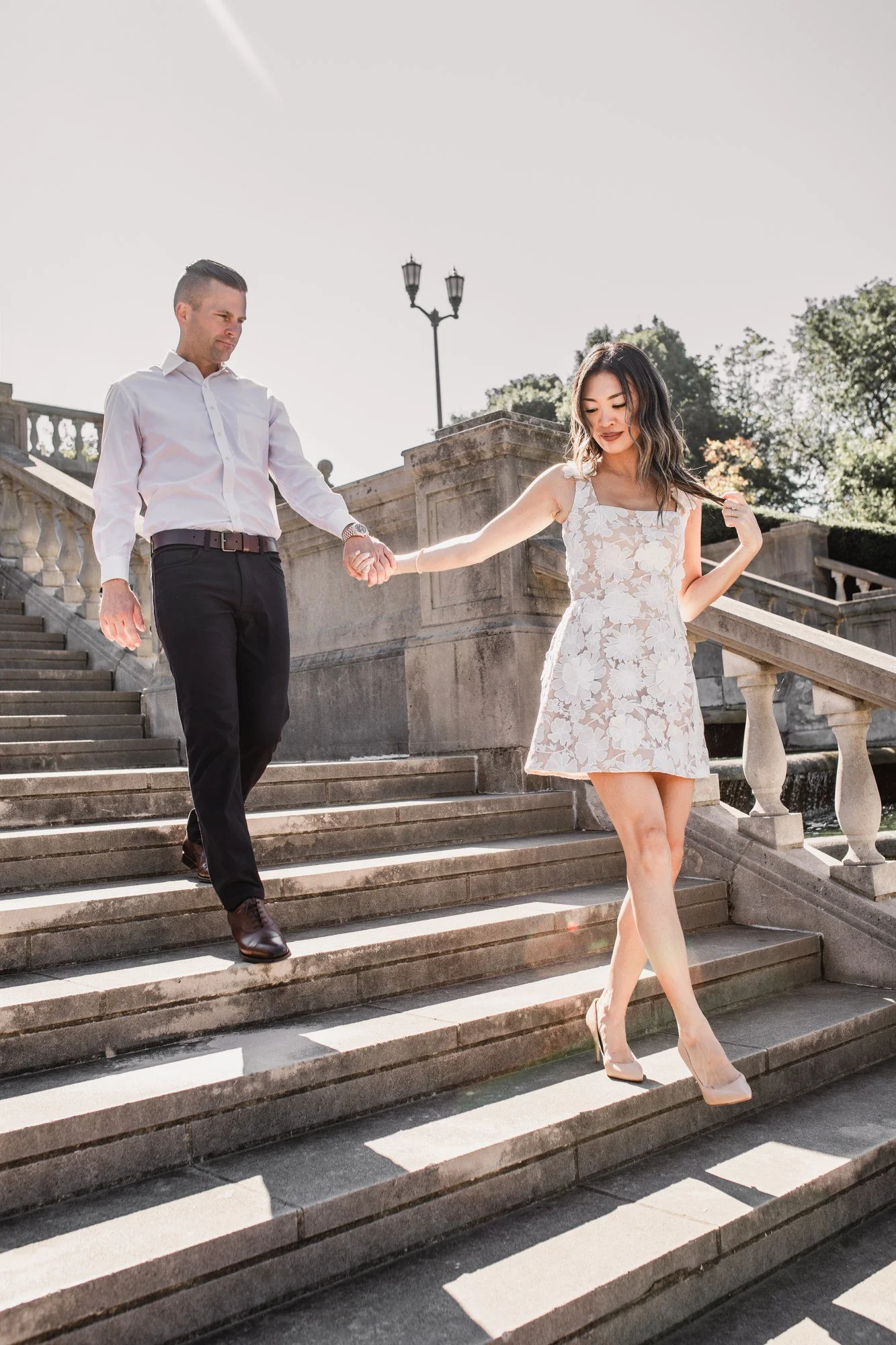 Kitty and Scott walking hand in hand down sunlit stone steps.