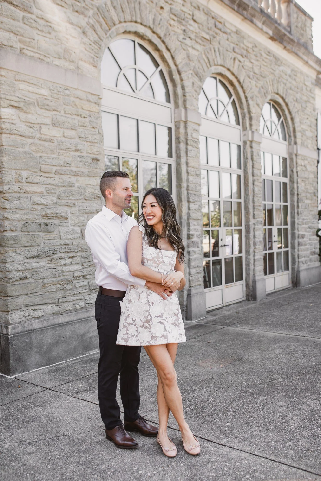 Kitty and Scott embracing in front of tall arched windows set in a stone facade.