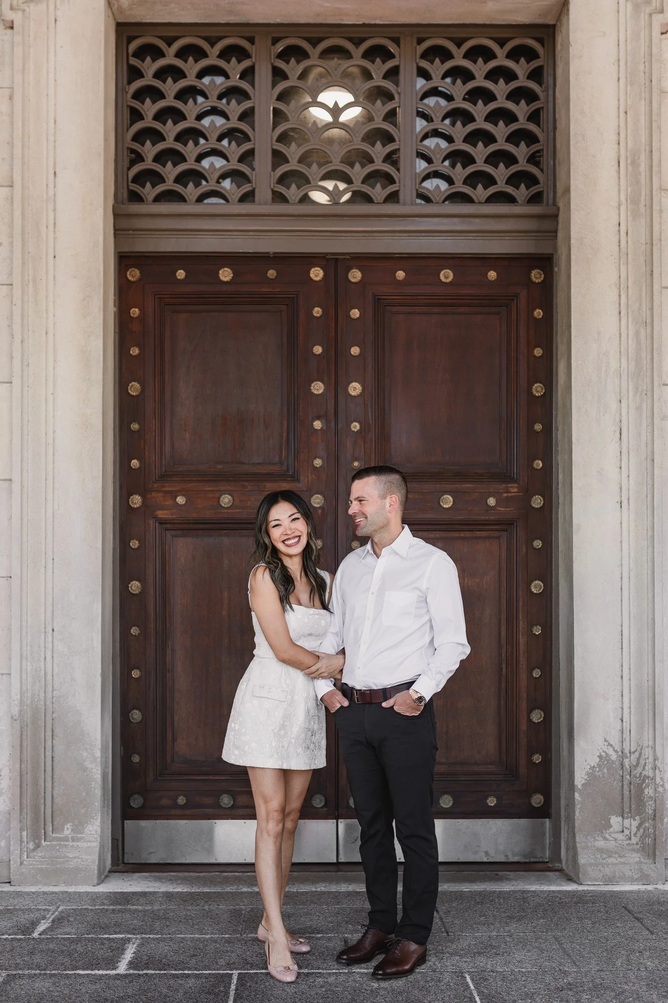 Kitty and Scott smiling together in front of tall wooden doors framed by carved stone.