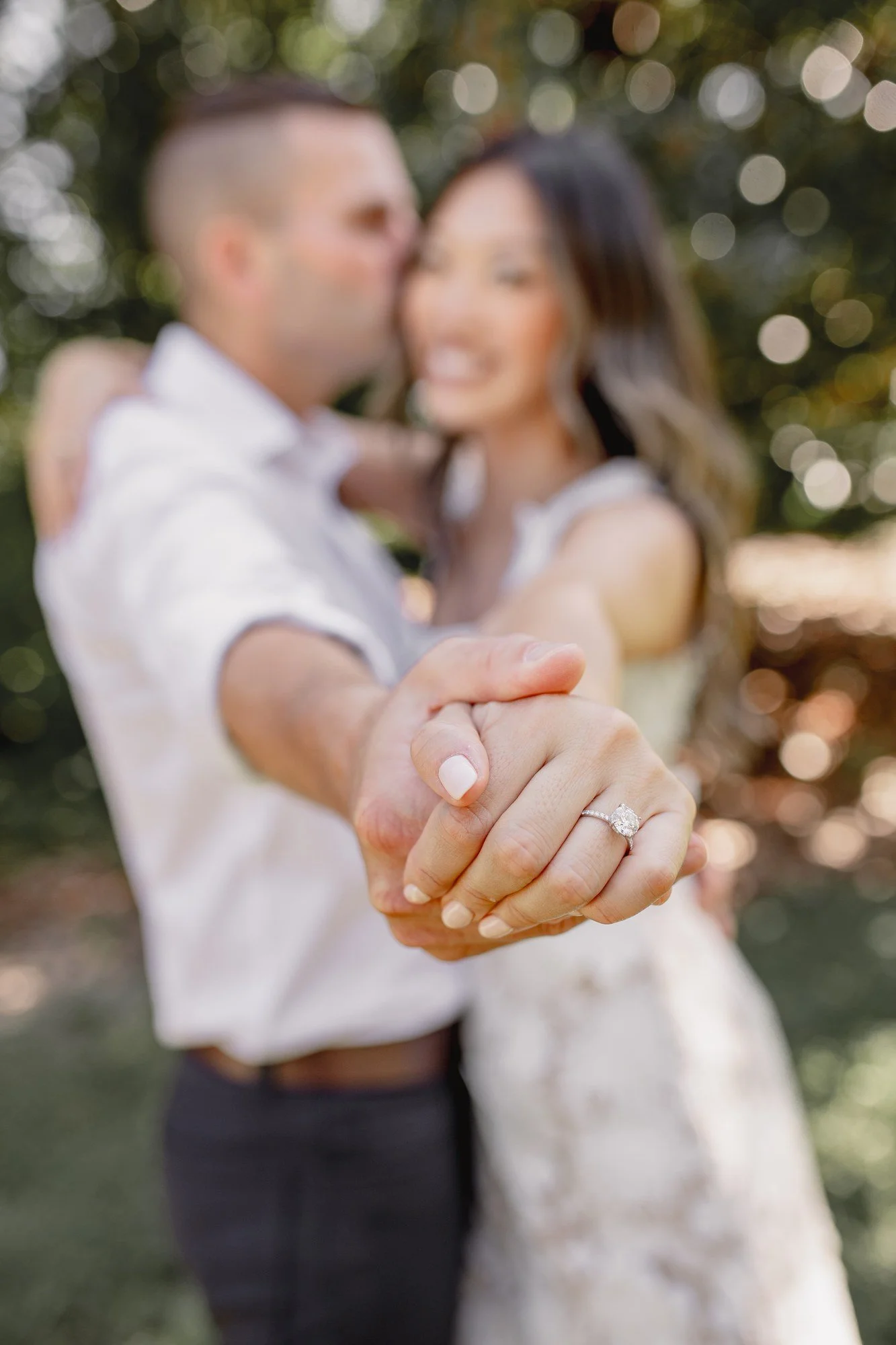 Kitty and Scott’s joined hands and engagement ring in focus, with the couple softly blurred behind them.