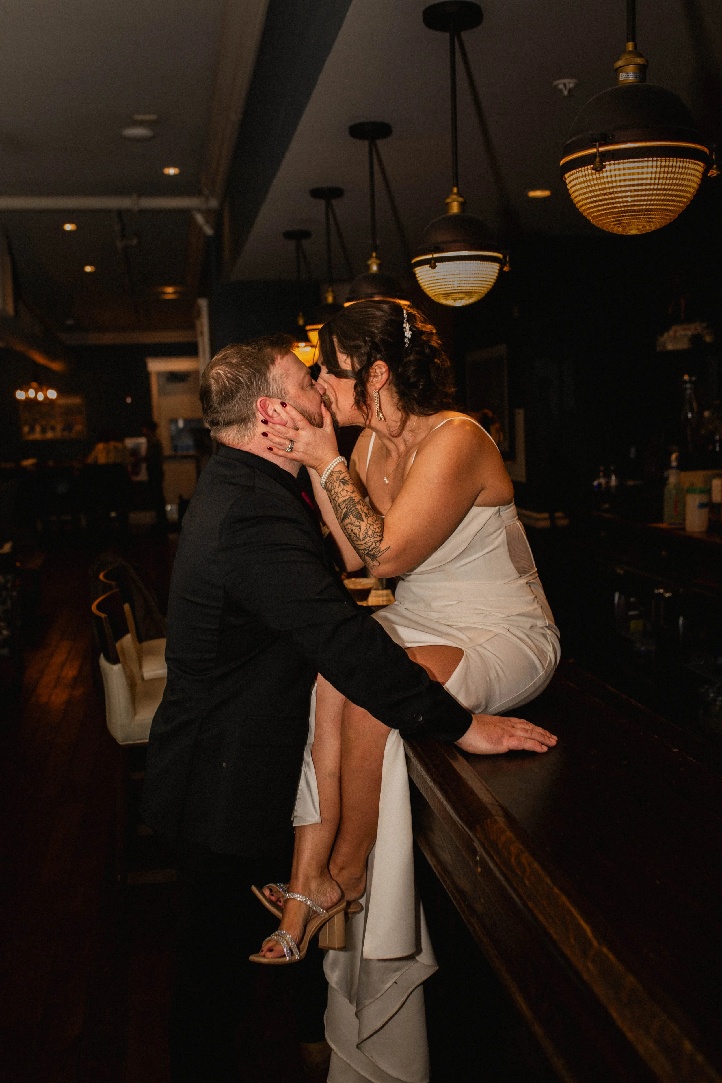 Bride sitting on the bar kissing groom during their wedding reception at The Landing Event Center in Loveland.