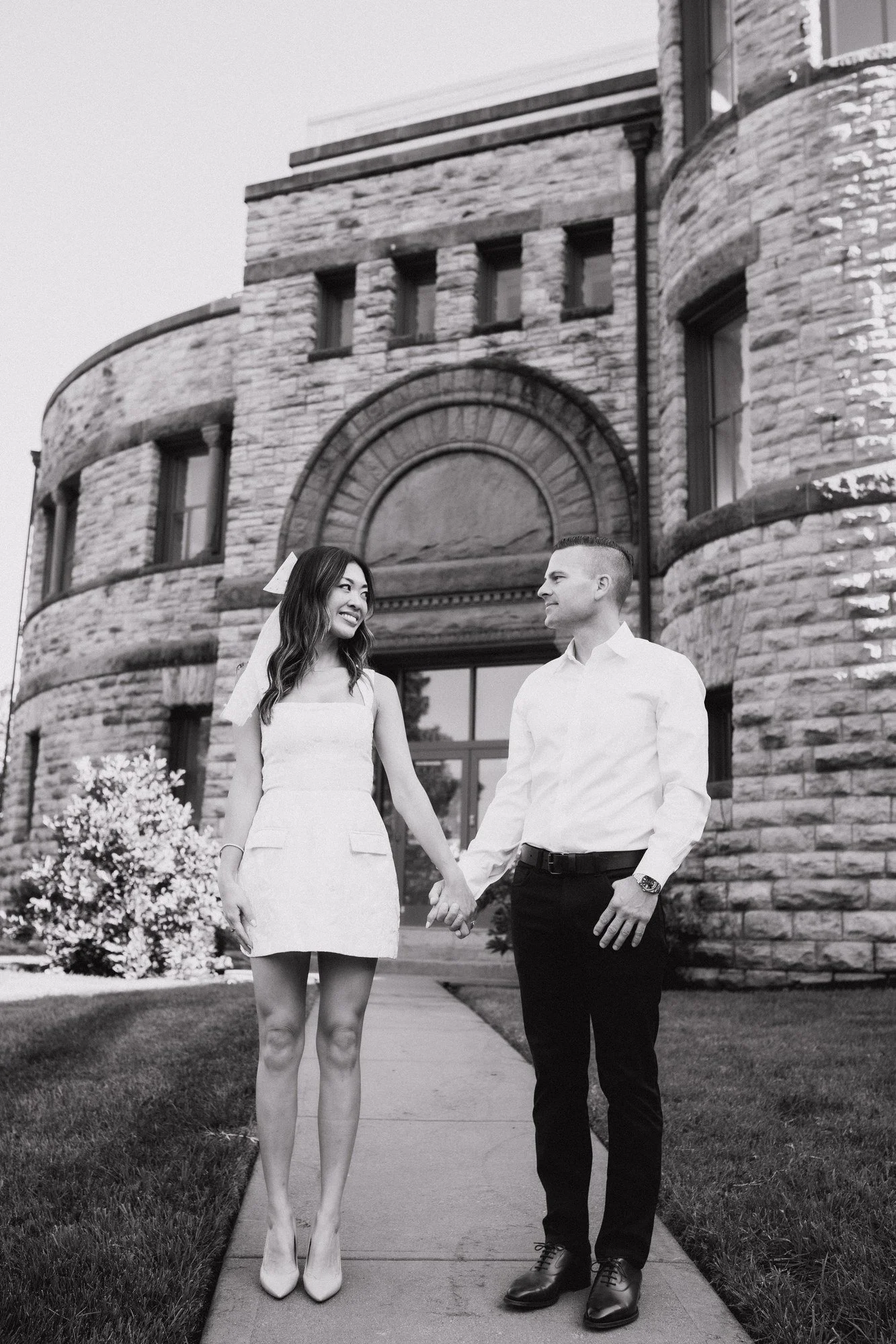 Black-and-white portrait of Kitty and Scott standing hand in hand outside the museum’s arched entrance.