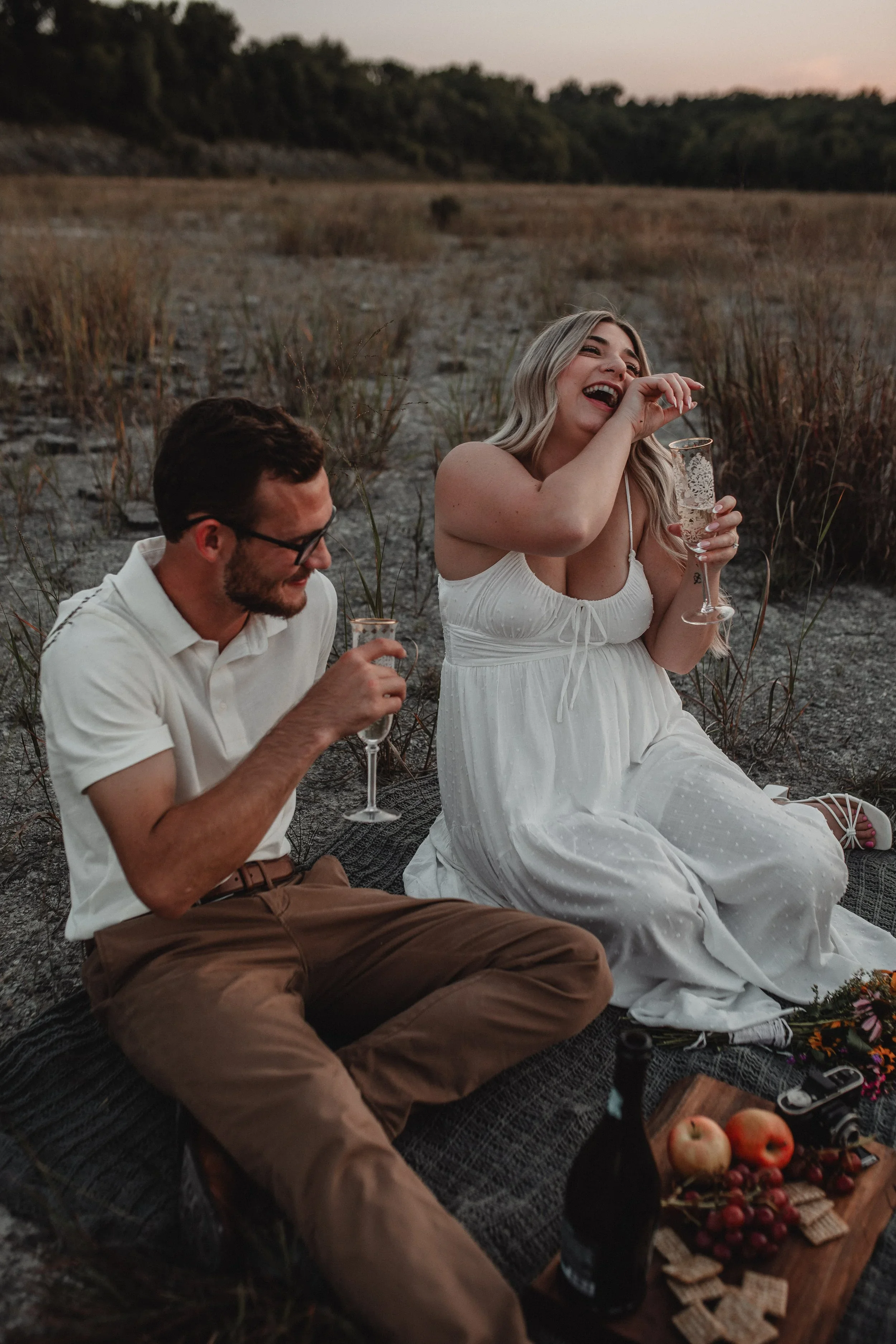 Engaged couple smiling together with champagne during an outdoor Cincinnati engagement session photographed by Sarah and Jordan of Every Atom Photography