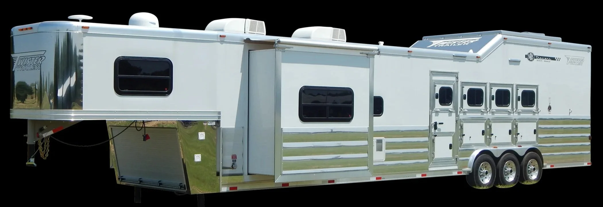 A large white horse trailer with multiple windows, dual axles, and various compartments, parked on grass with water in the background.