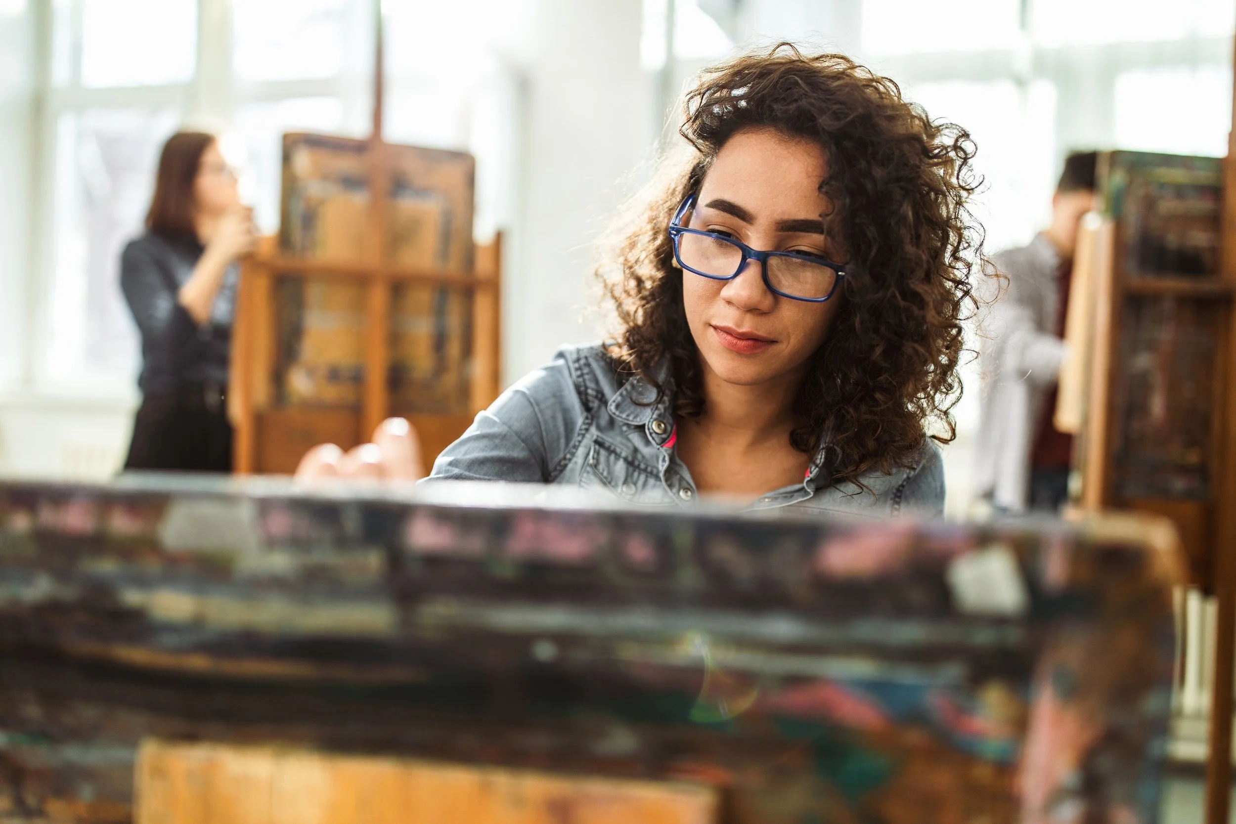 A person seated at an easel in a studio, working on a painting.