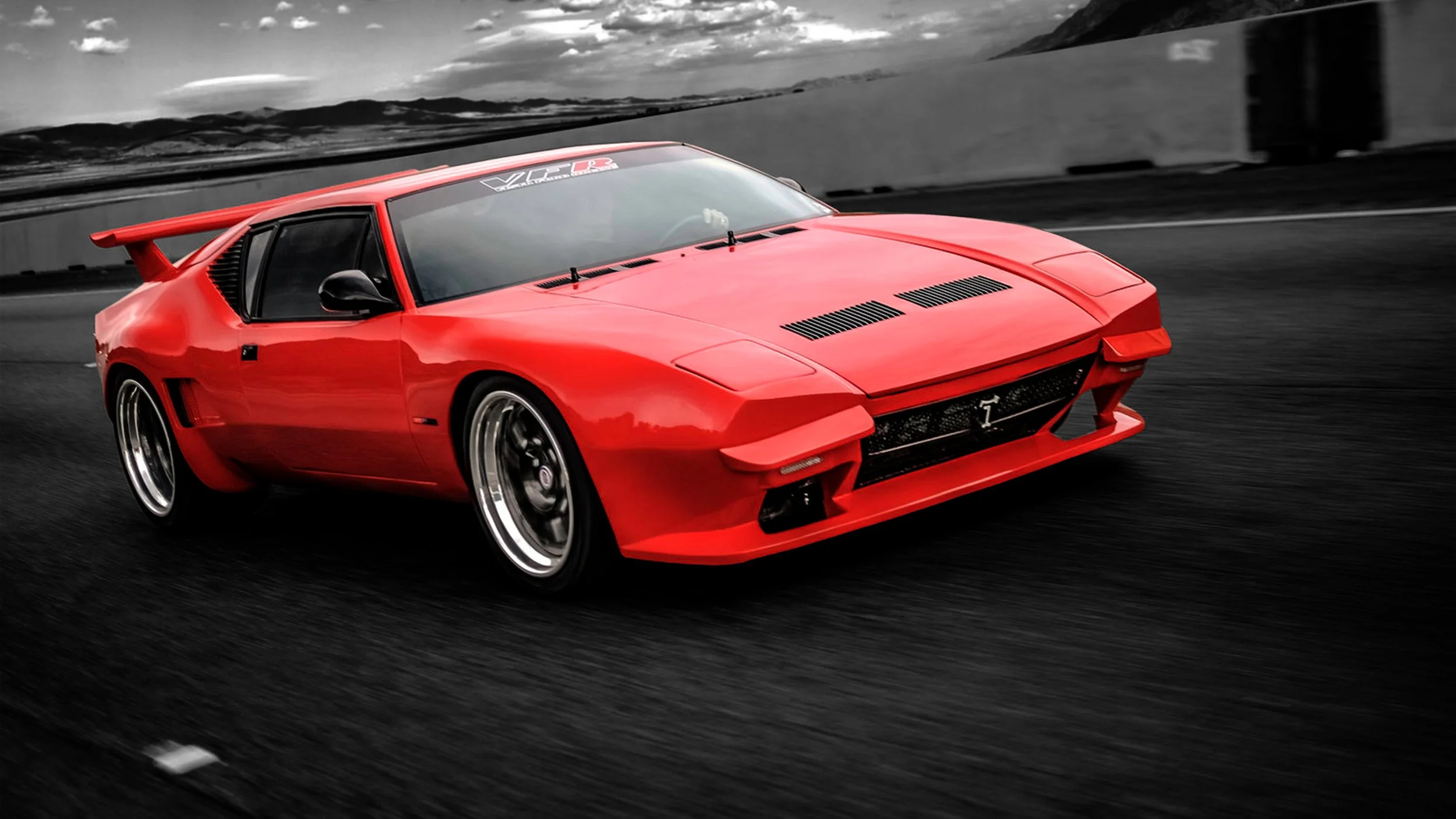 A red sports car speeding on a highway with a black and white background of mountains and clouds.