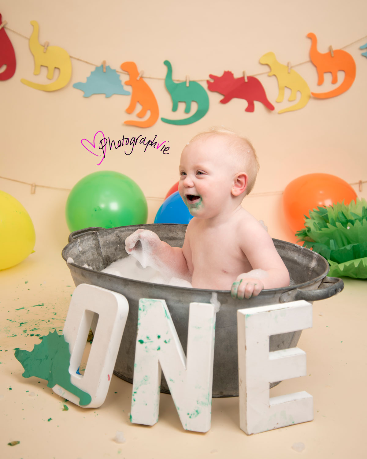 Cake_smash_photography_Ely_Cambridgeshire_first_birthday_dinosaur_themed_boy_in_tin_bath_looking_away_from_camera.jpg