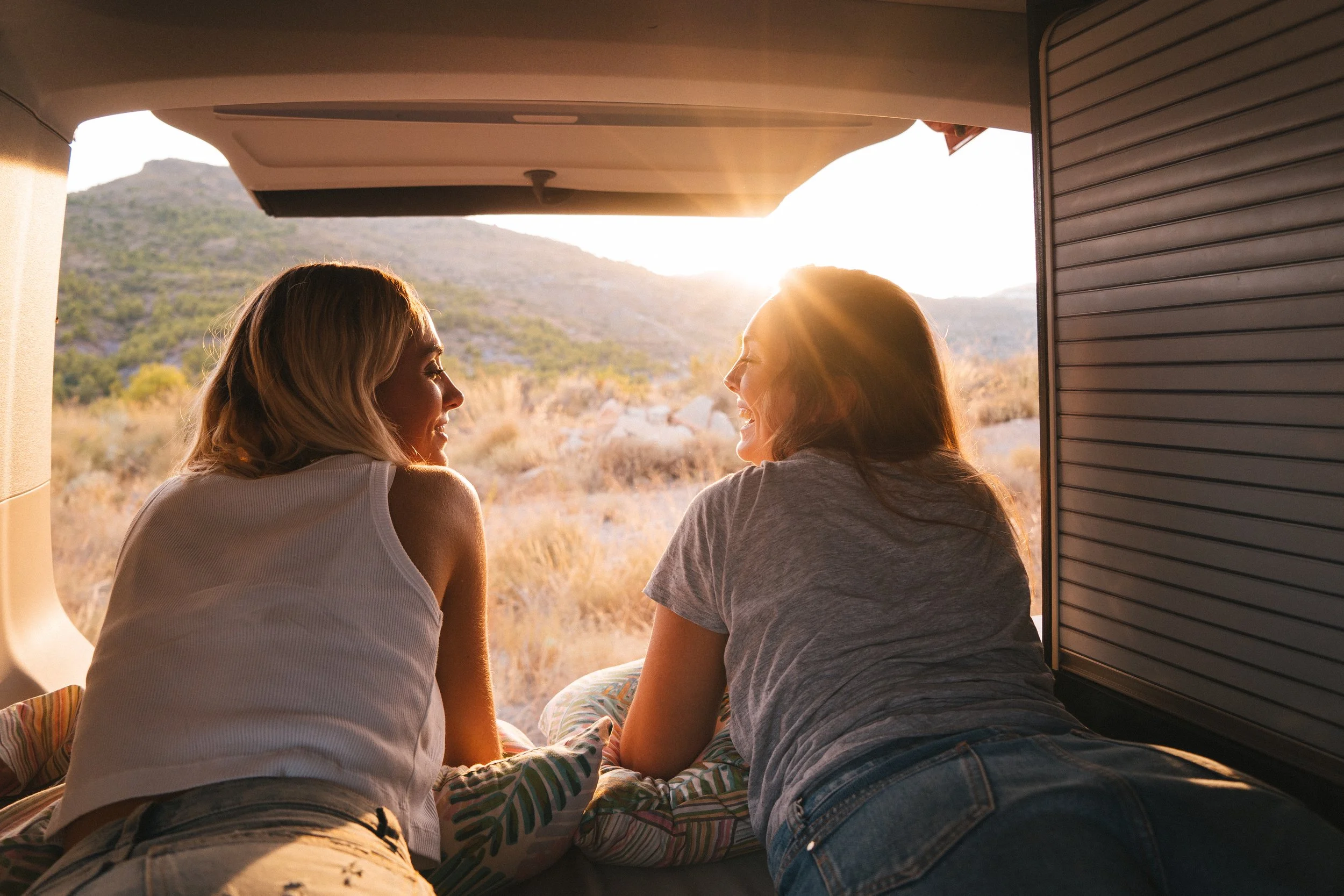 Two women smiling at each other during a camper-van sunset