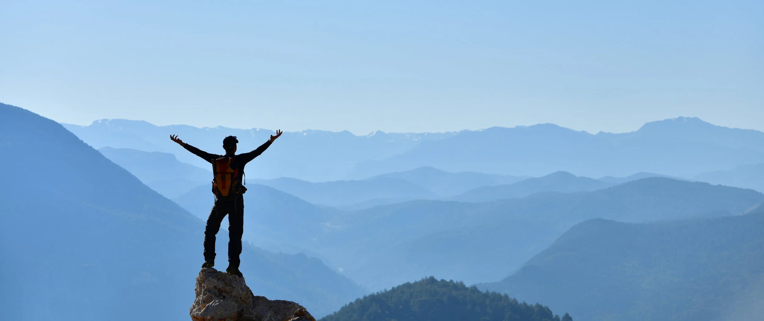 Person standing on a mountain peak with arms raised in freedom