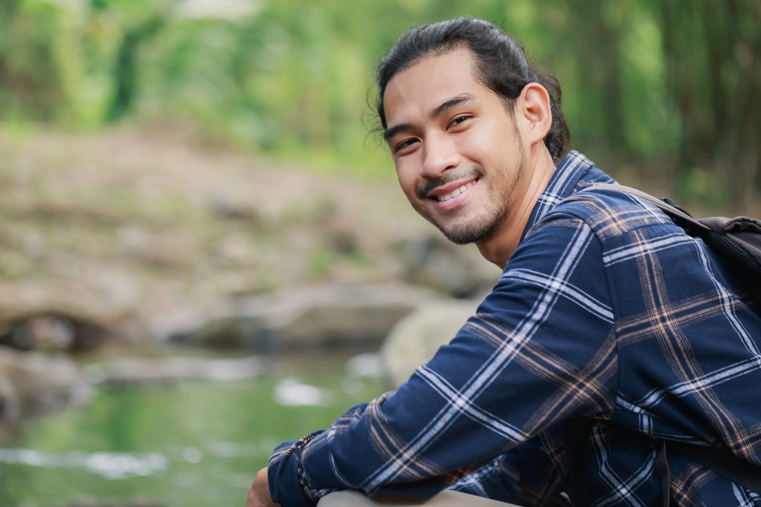 Smiling young man relaxing outdoors by a stream