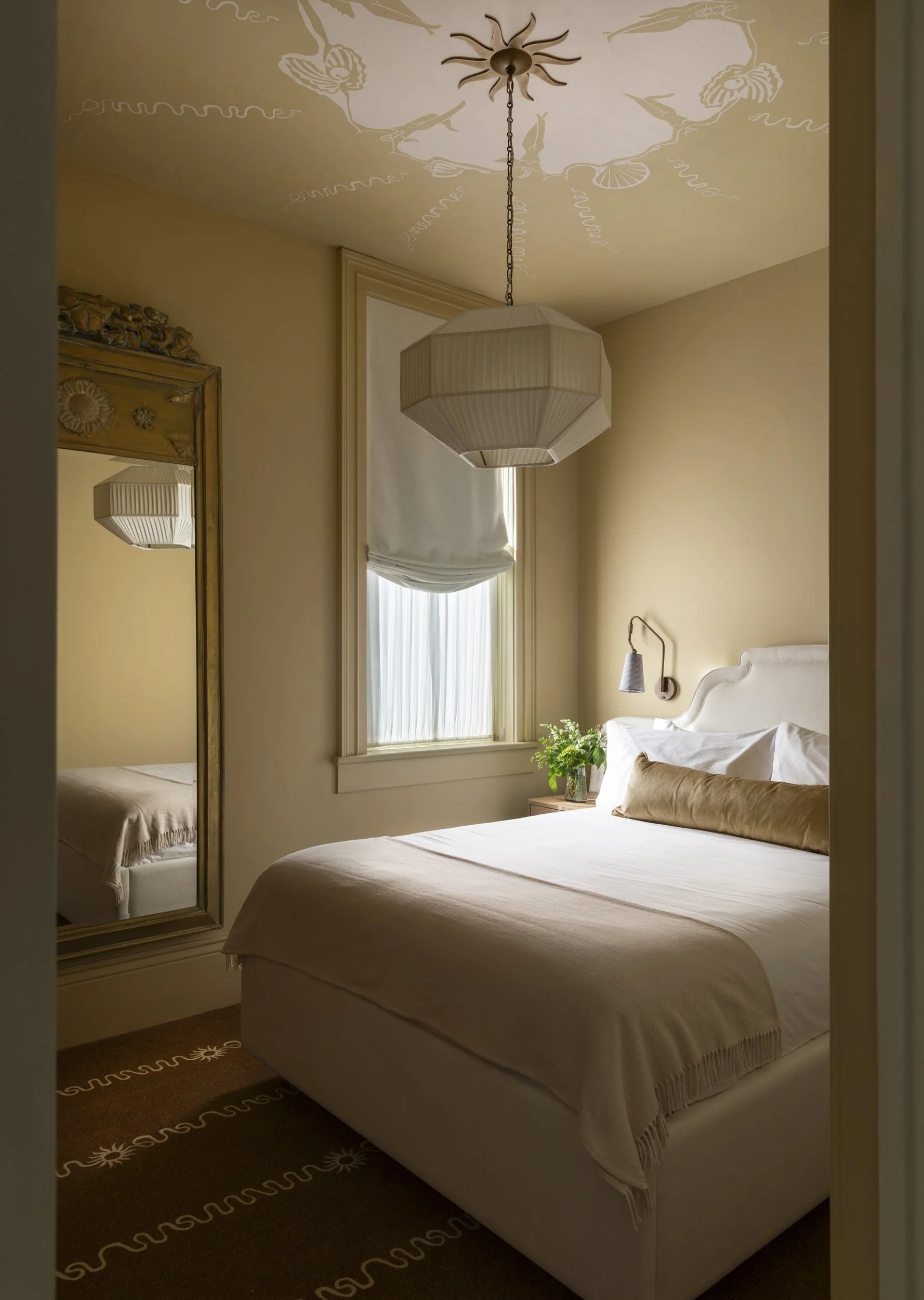 Guestroom with lantern light, tall antique mirror and neutral bedding at the Perle