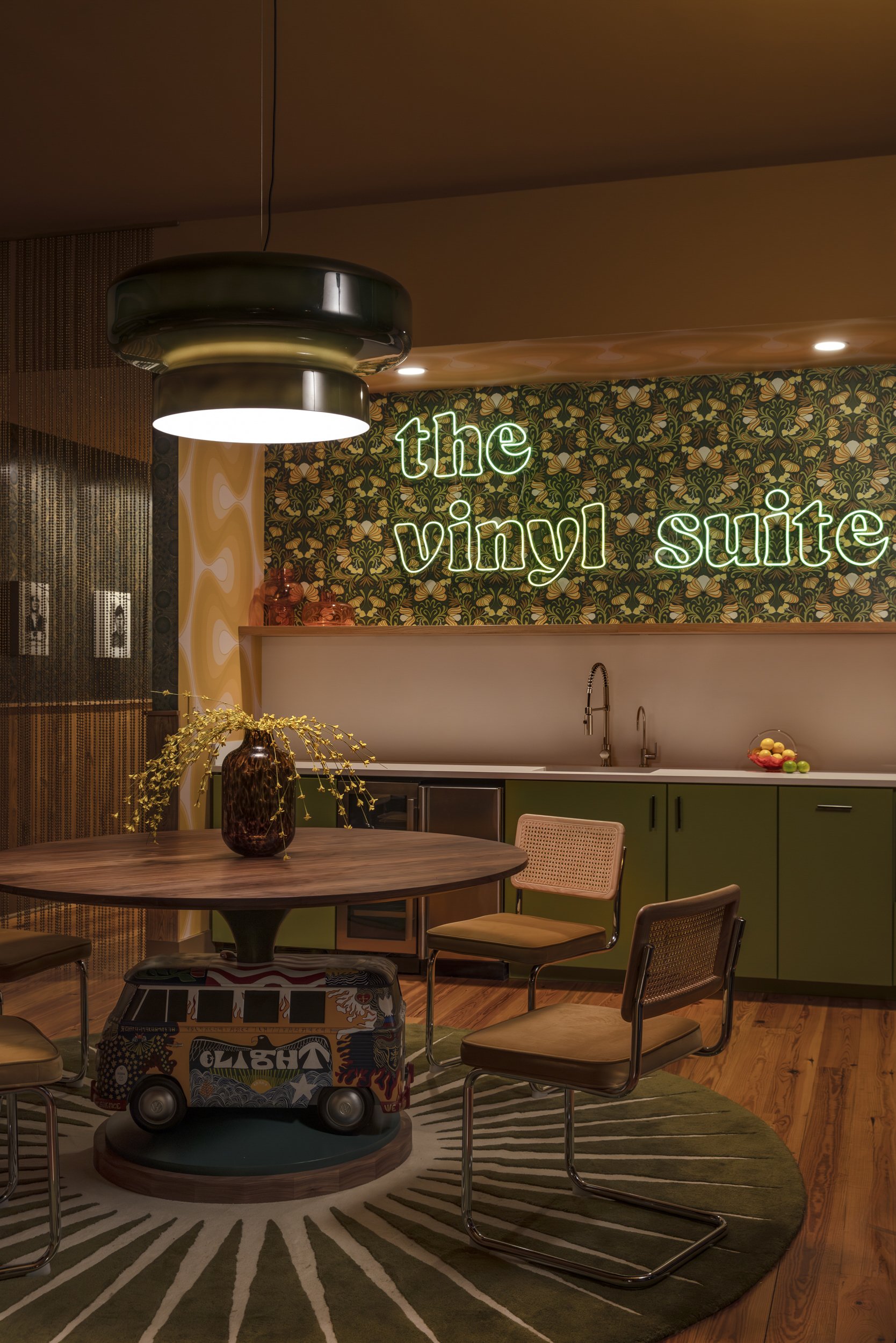Dining area with neon Vinyl Suite sign, olive cabinetry and sunburst rug at Copper Vine