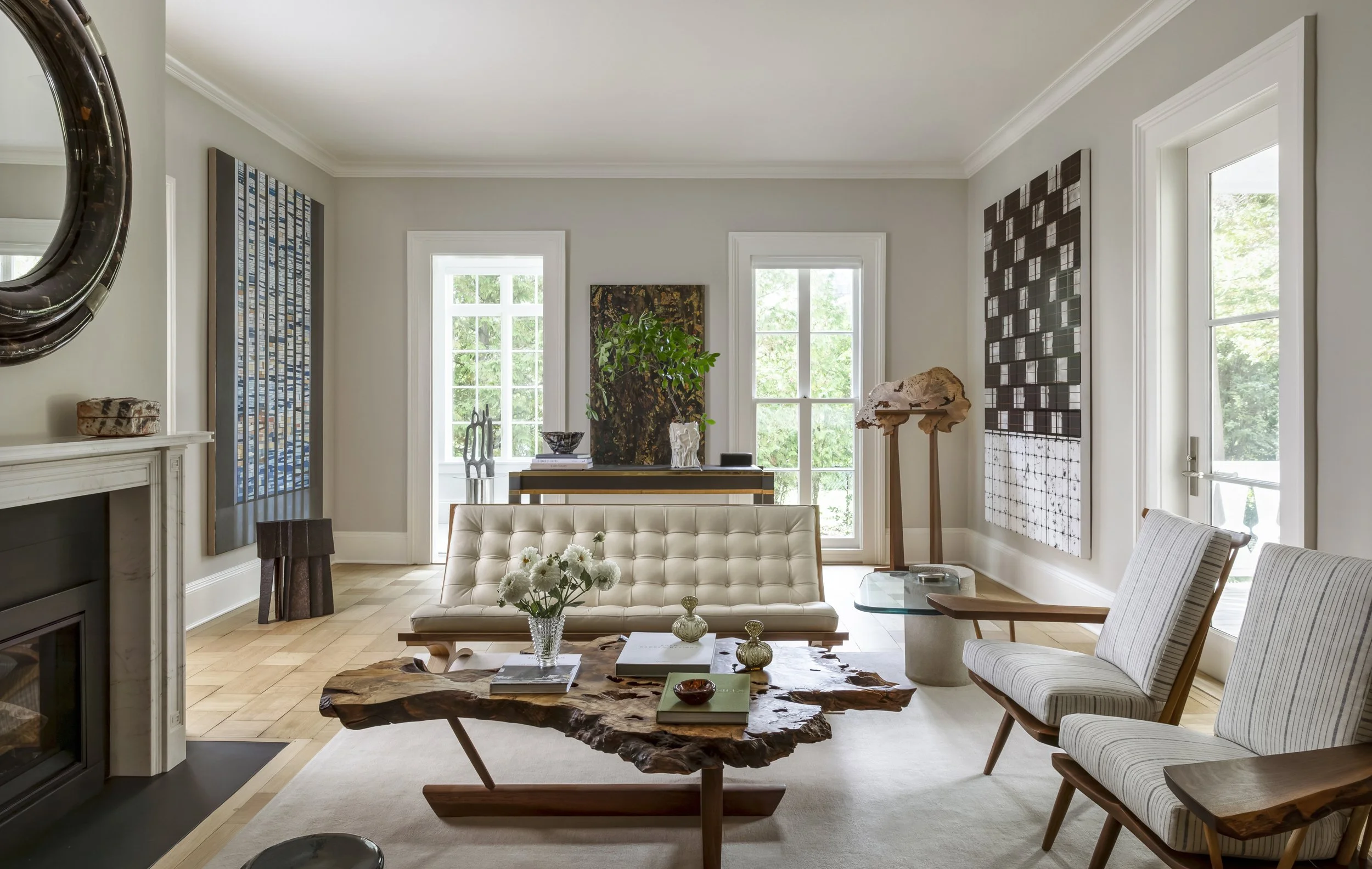 Living room with white walls and large windows, featuring artwork, a cream-colored tufted sofa, wooden furniture, and decorative objects.