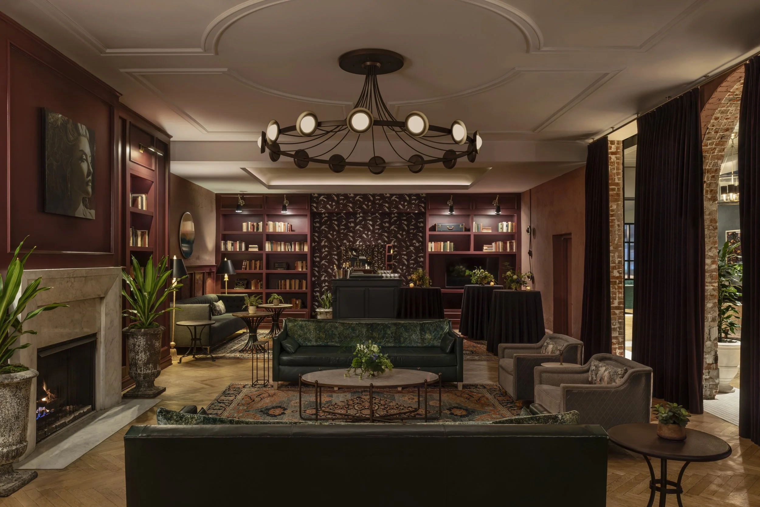 Library lounge with oxblood walls, bookshelves, green velvet sofa and marble fireplace at the Eliza Jane