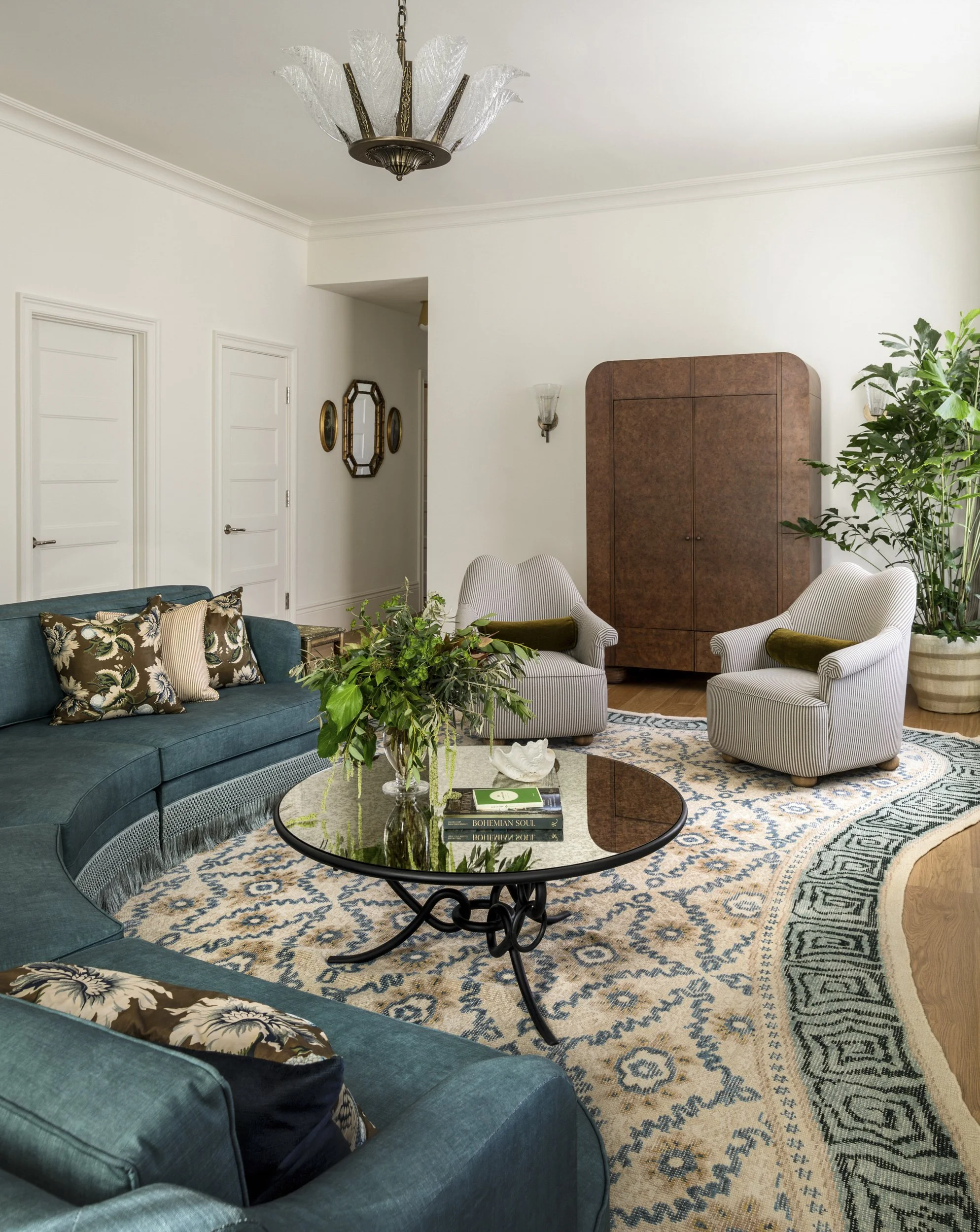 Suite living room with curved teal sectional, patterned rug and arched cabinet at the Perle