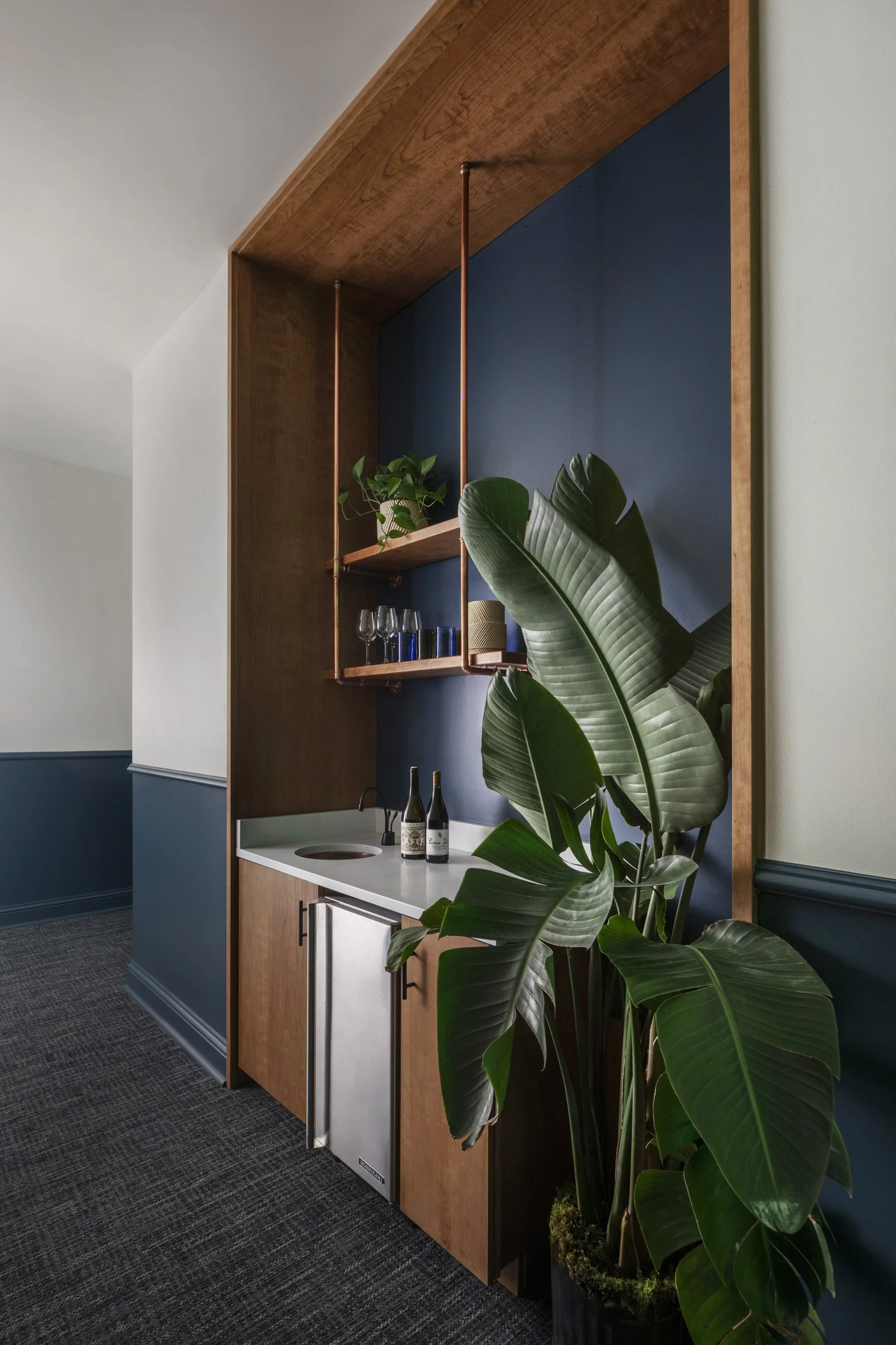 Wet bar with cherry millwork, navy walls and a large bird of paradise at Copper Vine
