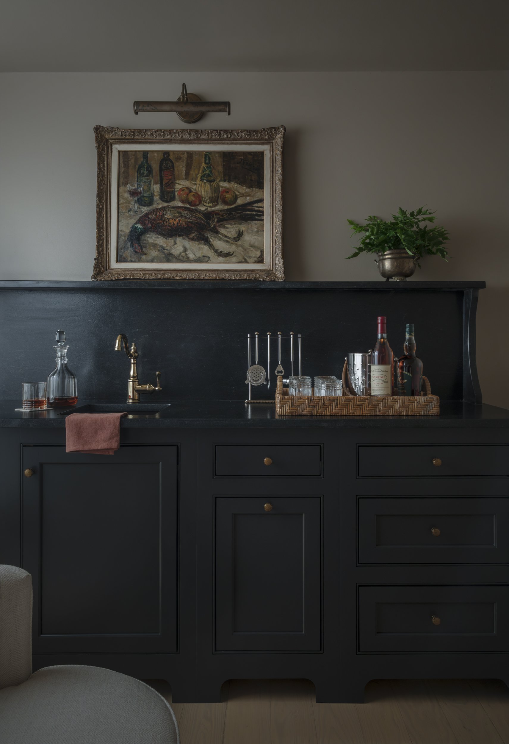 Black bar cabinetry with brass fixtures, decanters and a game-bird still life lit above at the Patterson