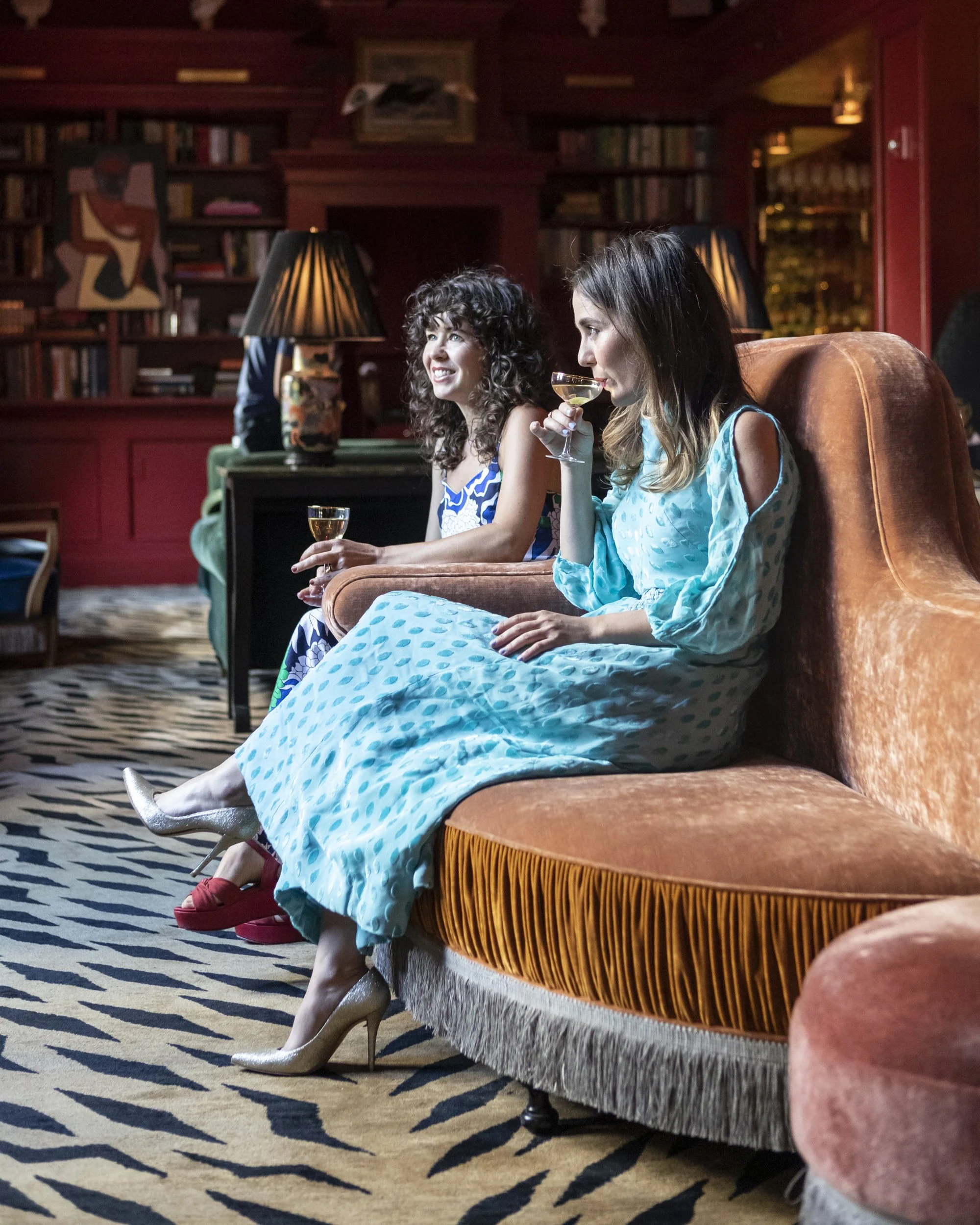 Two women with cocktails on a velvet sofa in the library bar at Bar Marilou, New Orleans