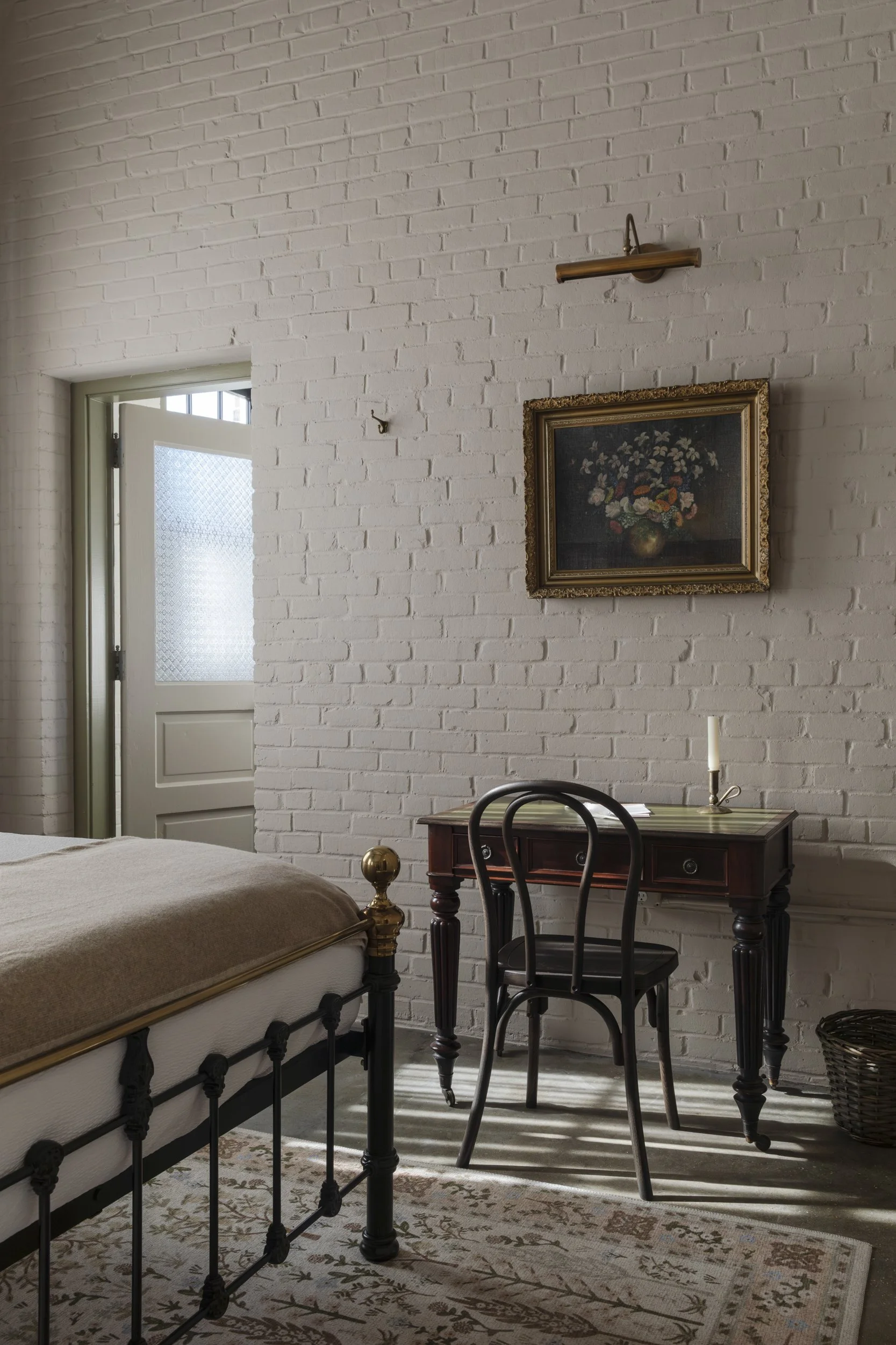 Guestroom with iron bed, whitewashed brick wall and gilt-framed still life at the Patterson