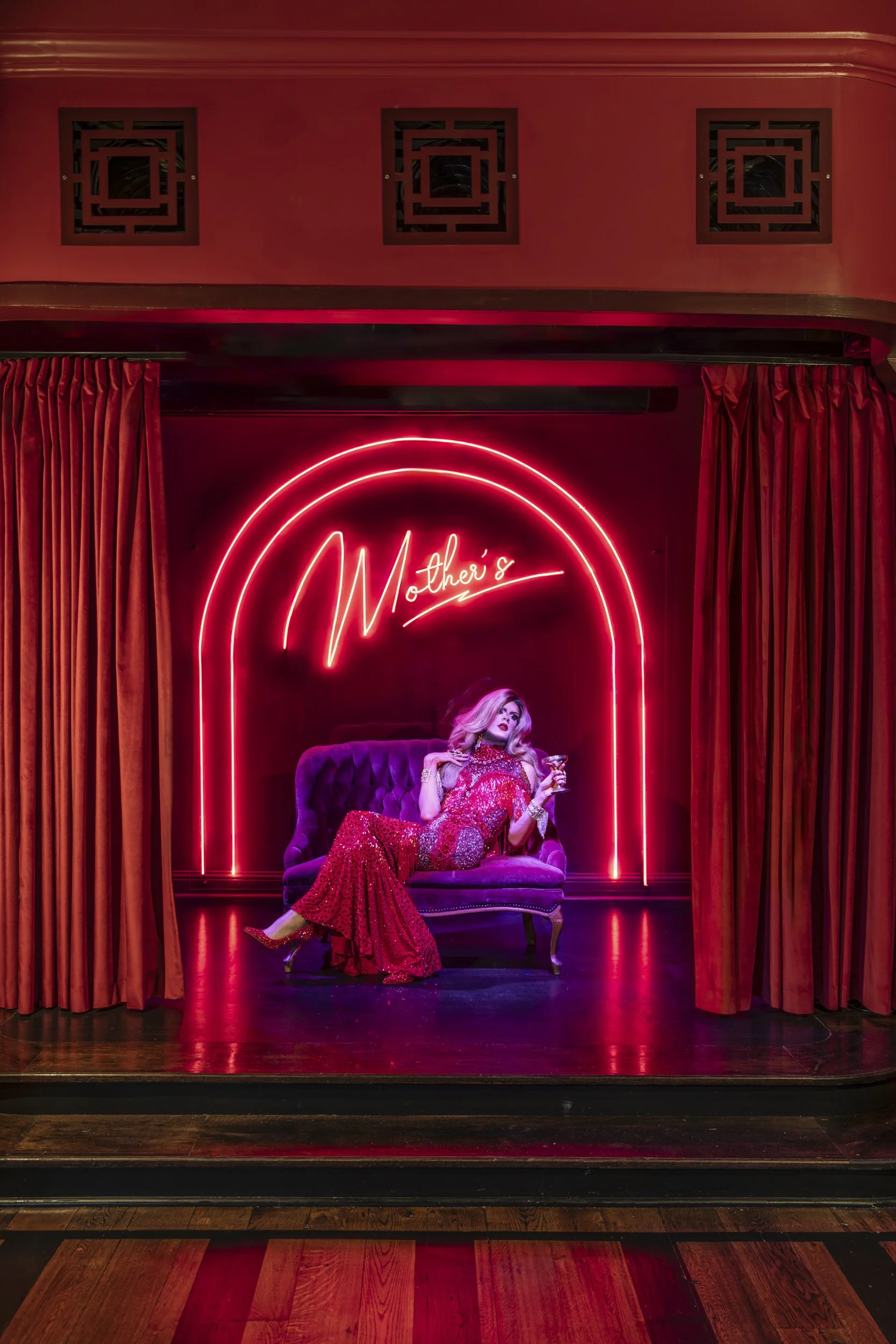 Performer in a red gown on a purple velvet settee beneath the neon sign at Mother’s,
Baton Rouge