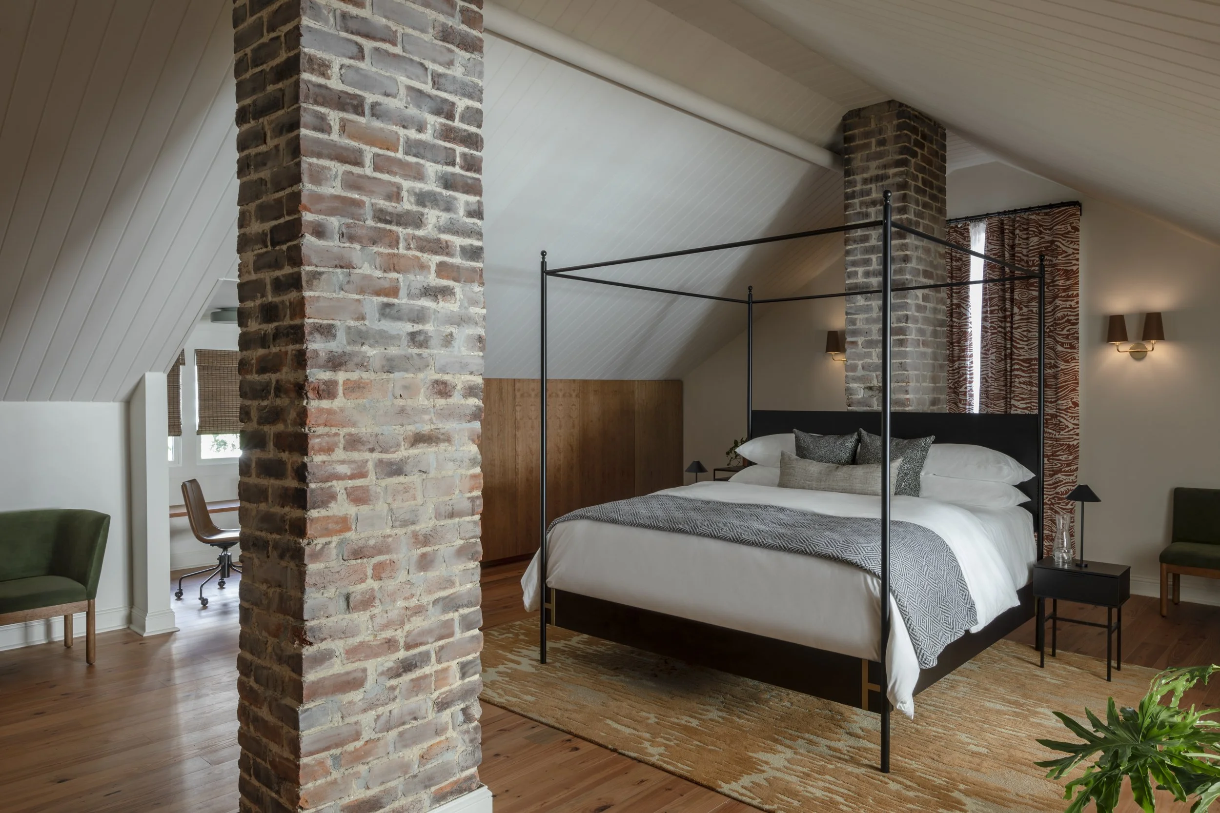 Guestroom with black canopy bed from Doorman Designs beside an exposed brick column at Copper Vine