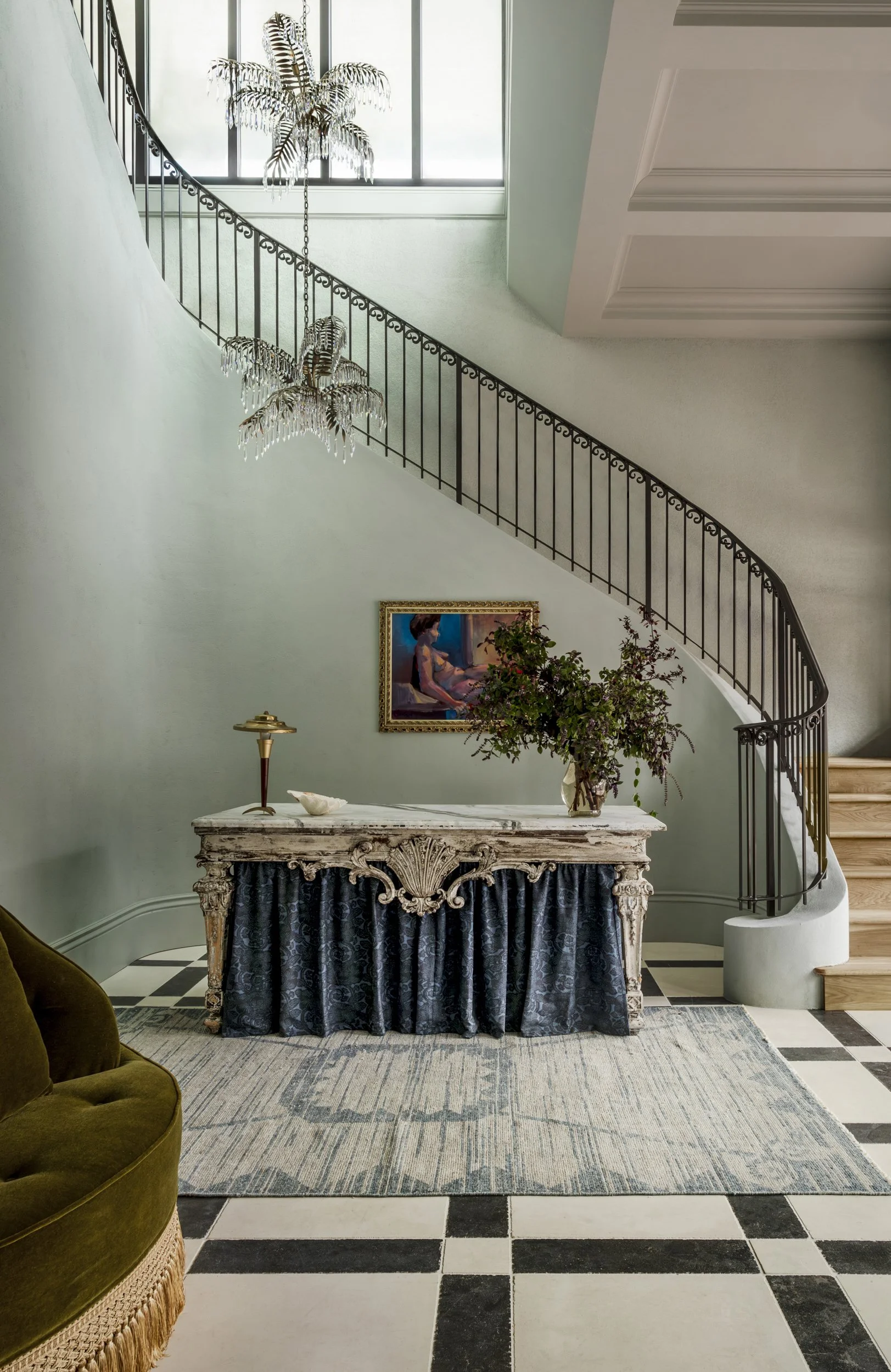 Curved staircase with iron railing and skirted console on a checkerboard marble floor at the Perle