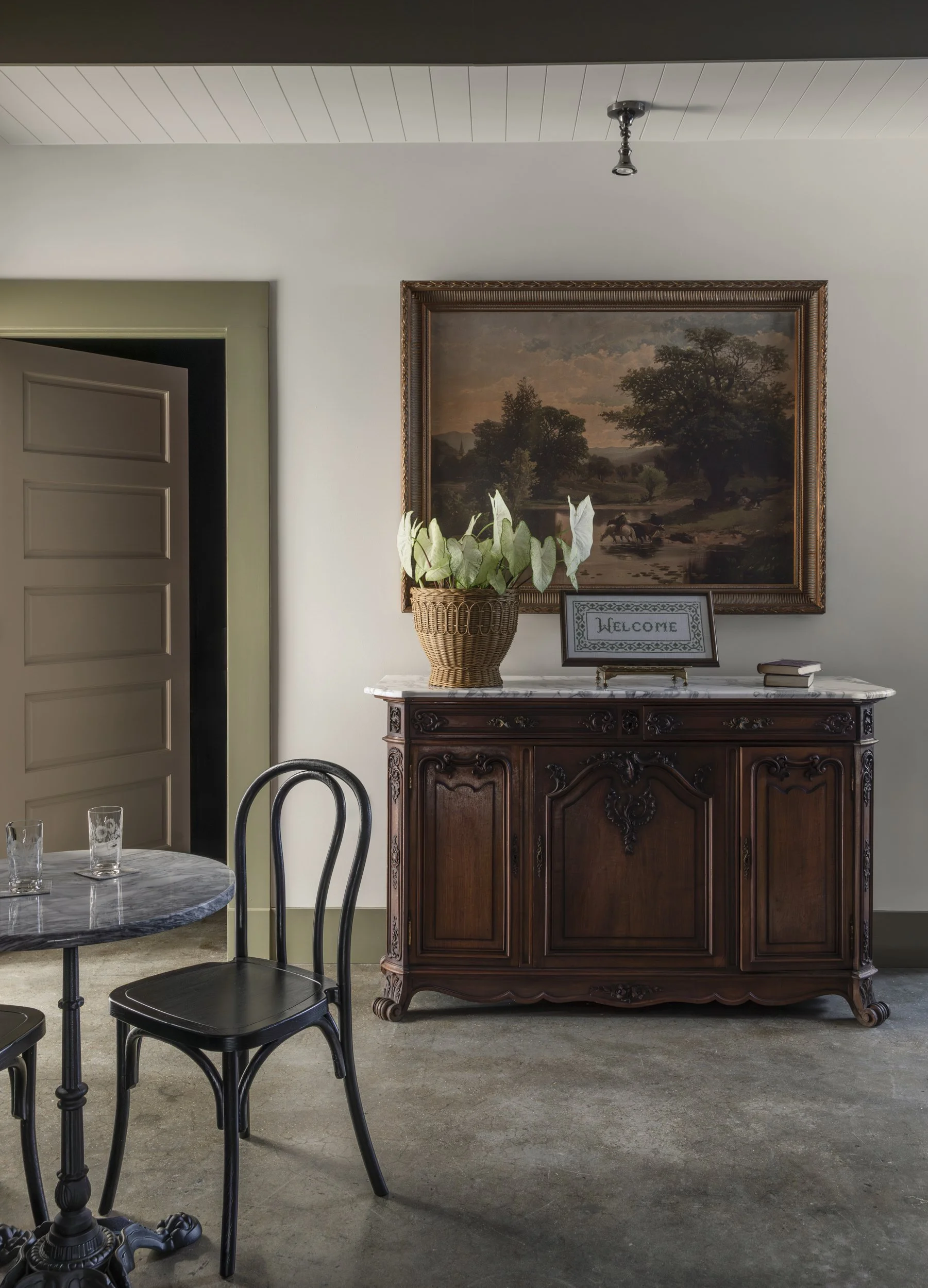 Carved sideboard beneath a gilt-framed landscape painting with marble bistro table at the Patterson