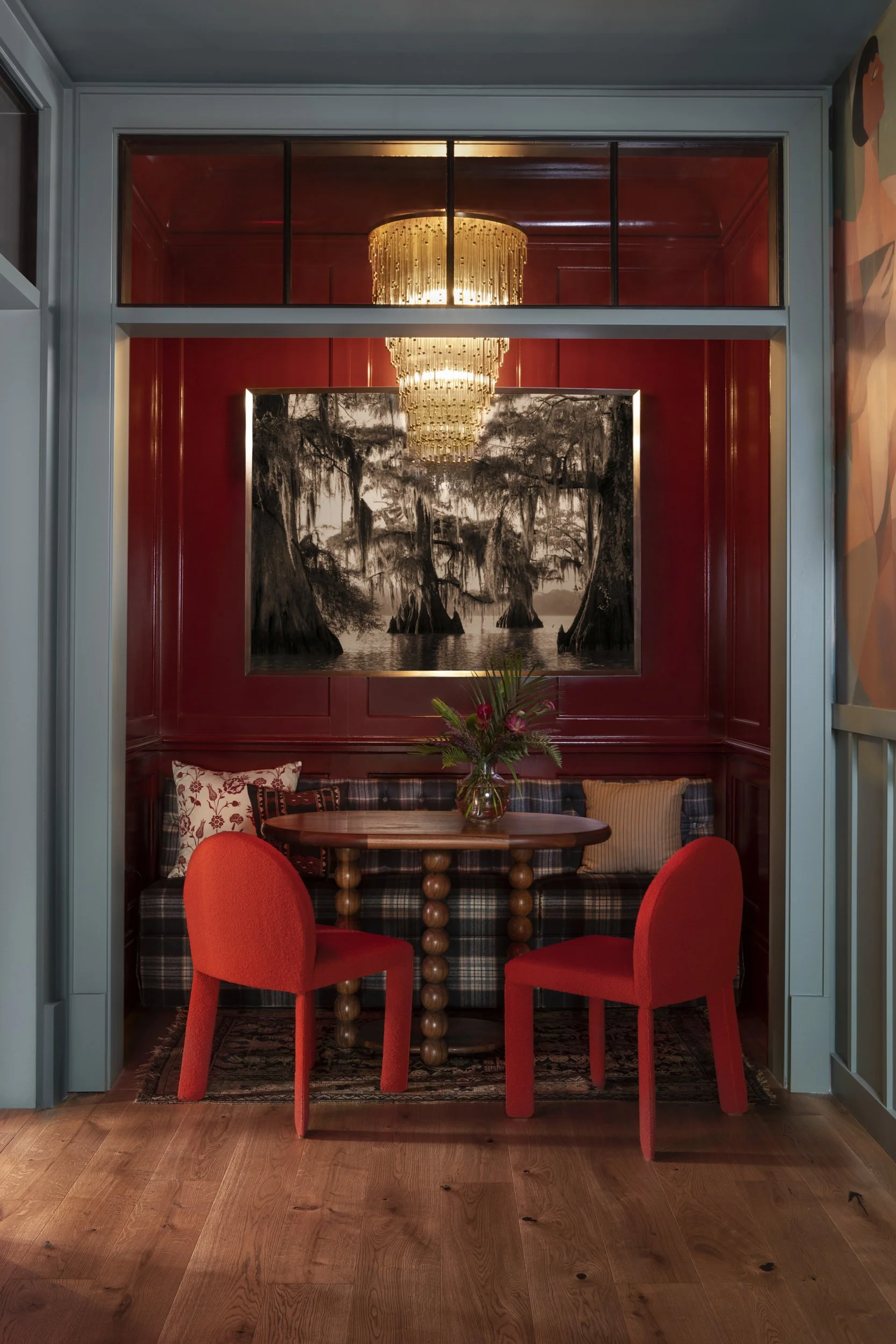 Red lacquered dining nook framed by a teal doorway with pleated pendant at Virgin Hotels New Orleans
