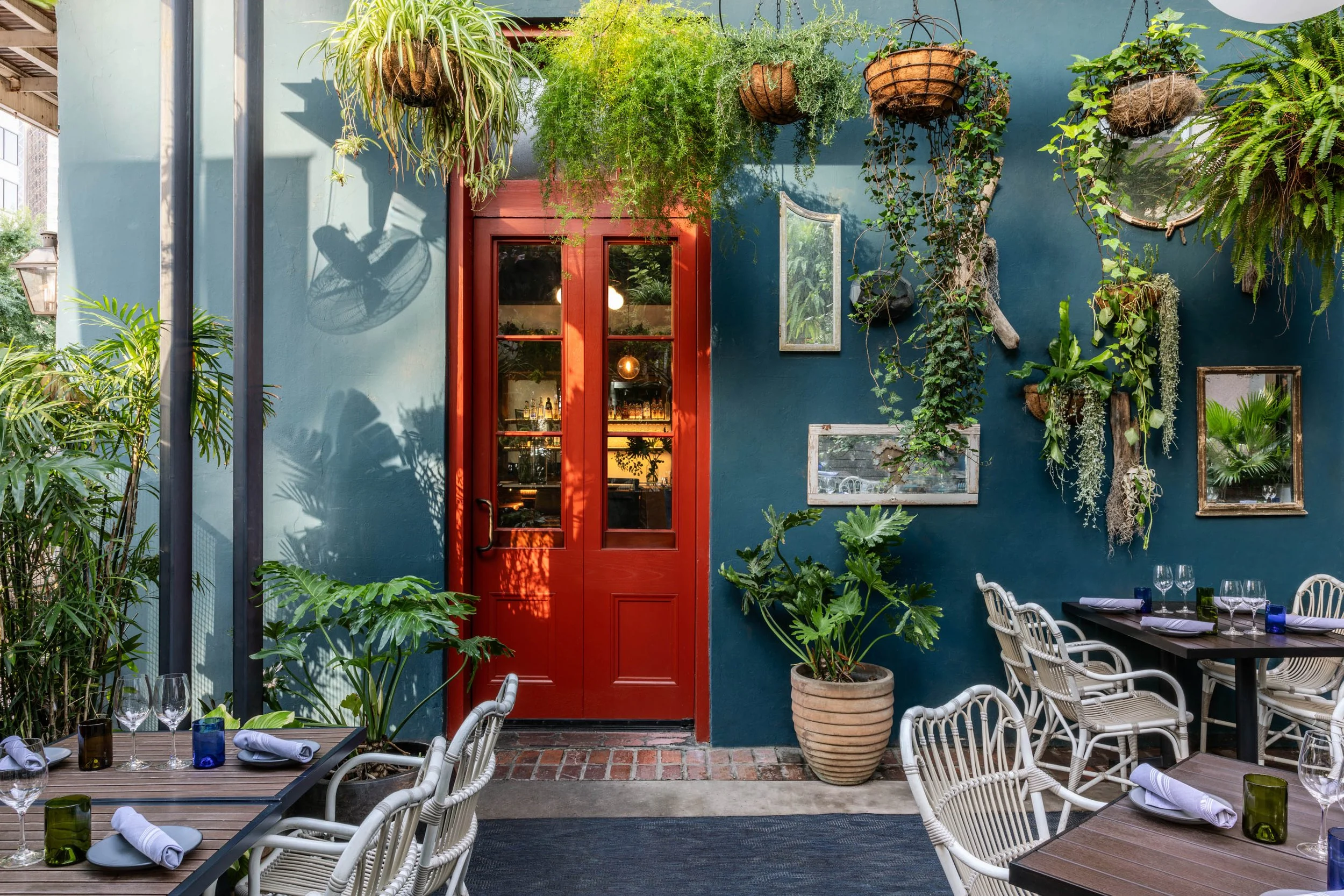 Red door and hanging plants against a blue courtyard wall at Copper Vine, New Orleans