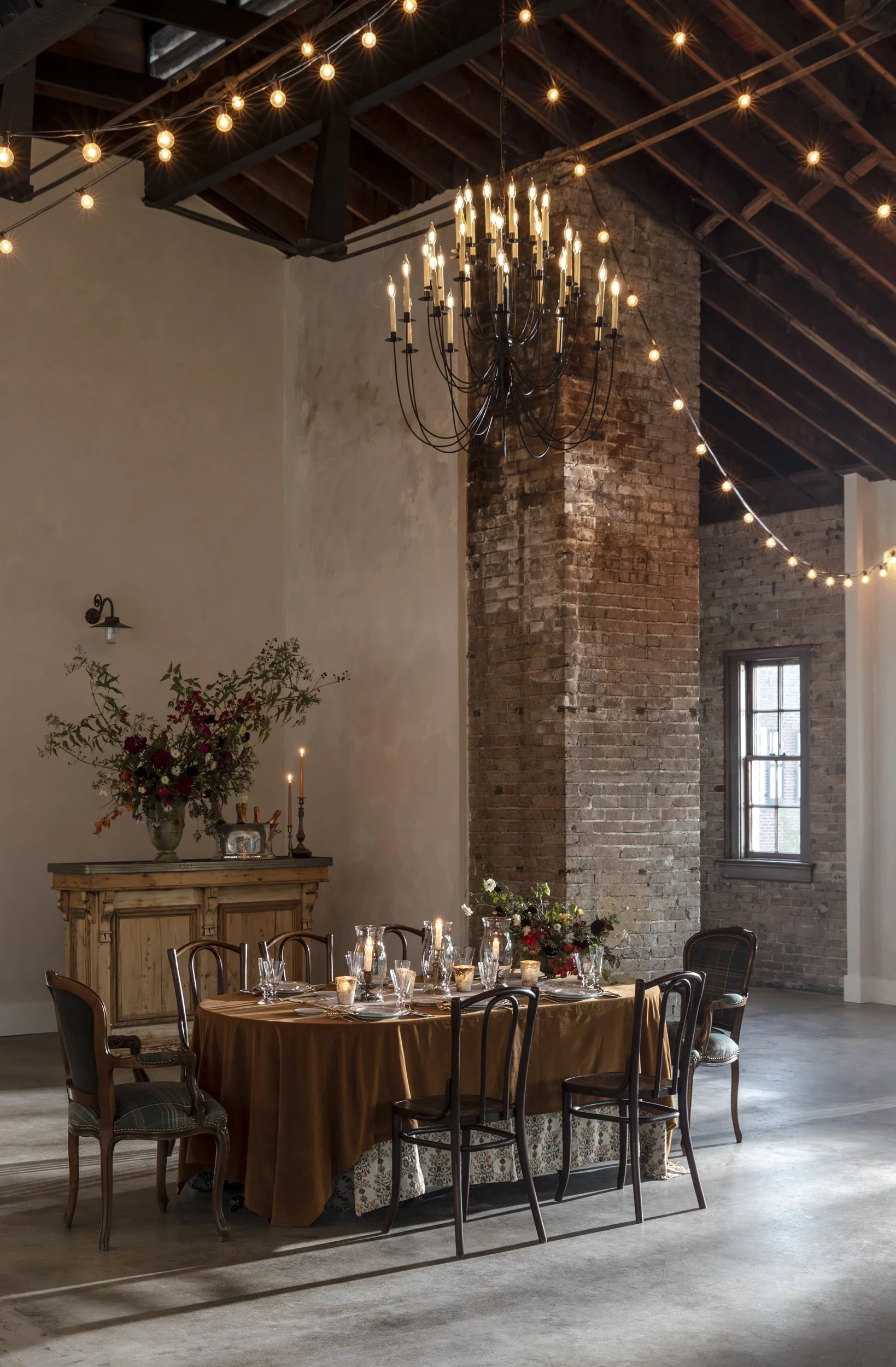 Event space with brick column, timber ceiling and string lights above a long table at the Patterson