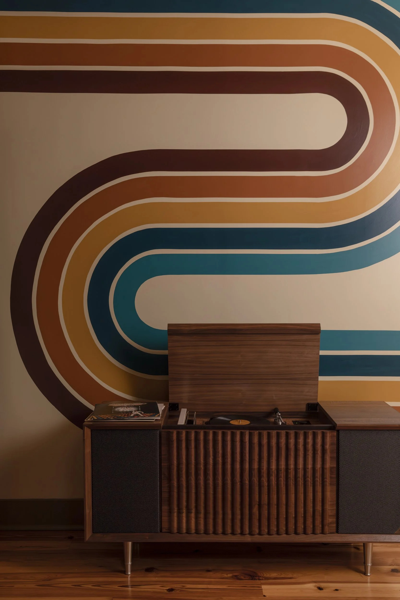 Walnut record console against a curved retro stripe mural on pine flooring in the Vinyl Room at Copper Vine