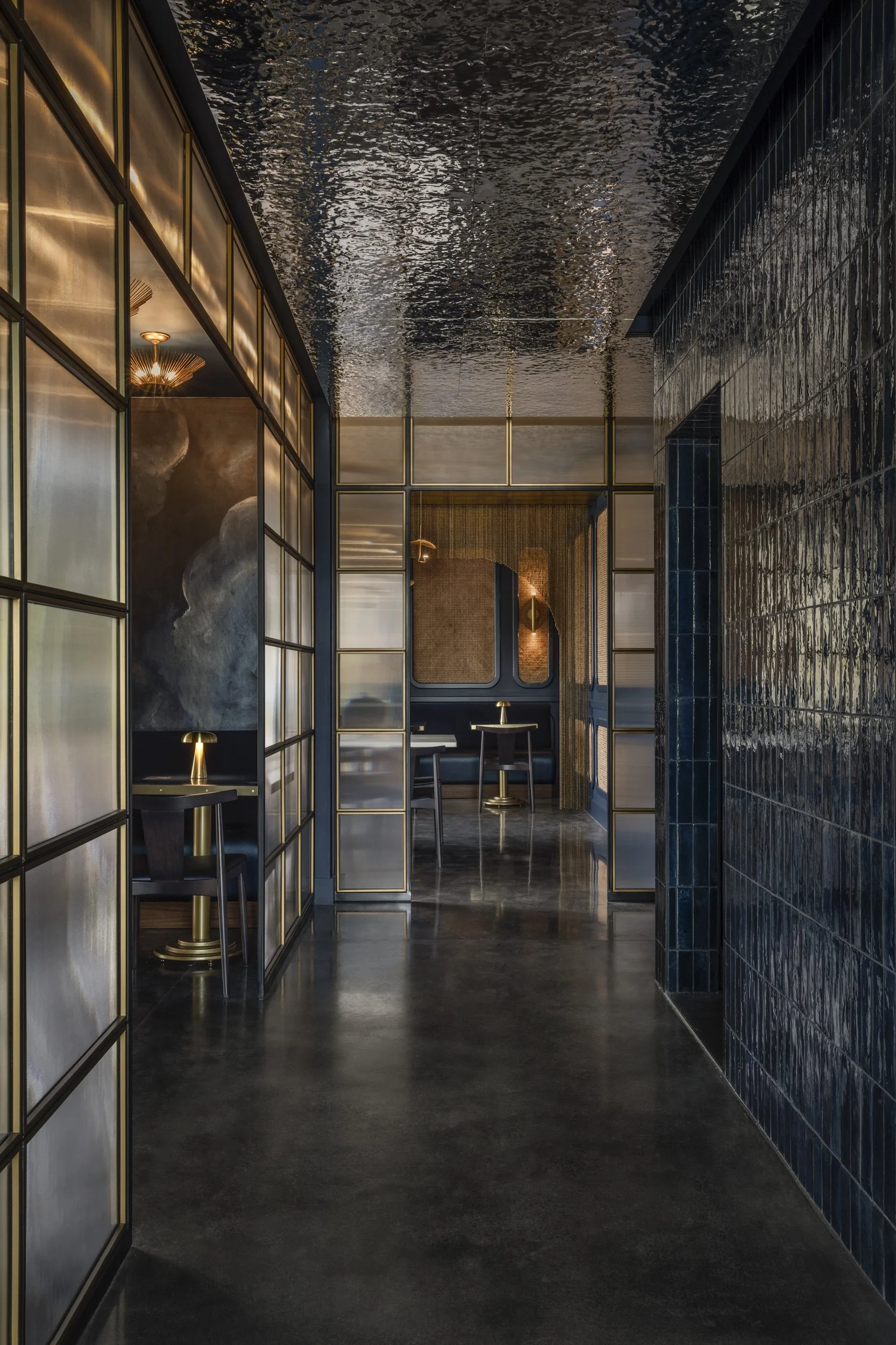 Corridor of brass-framed glass beneath a rippled glazed ceiling at Tsunami, Baton Rouge