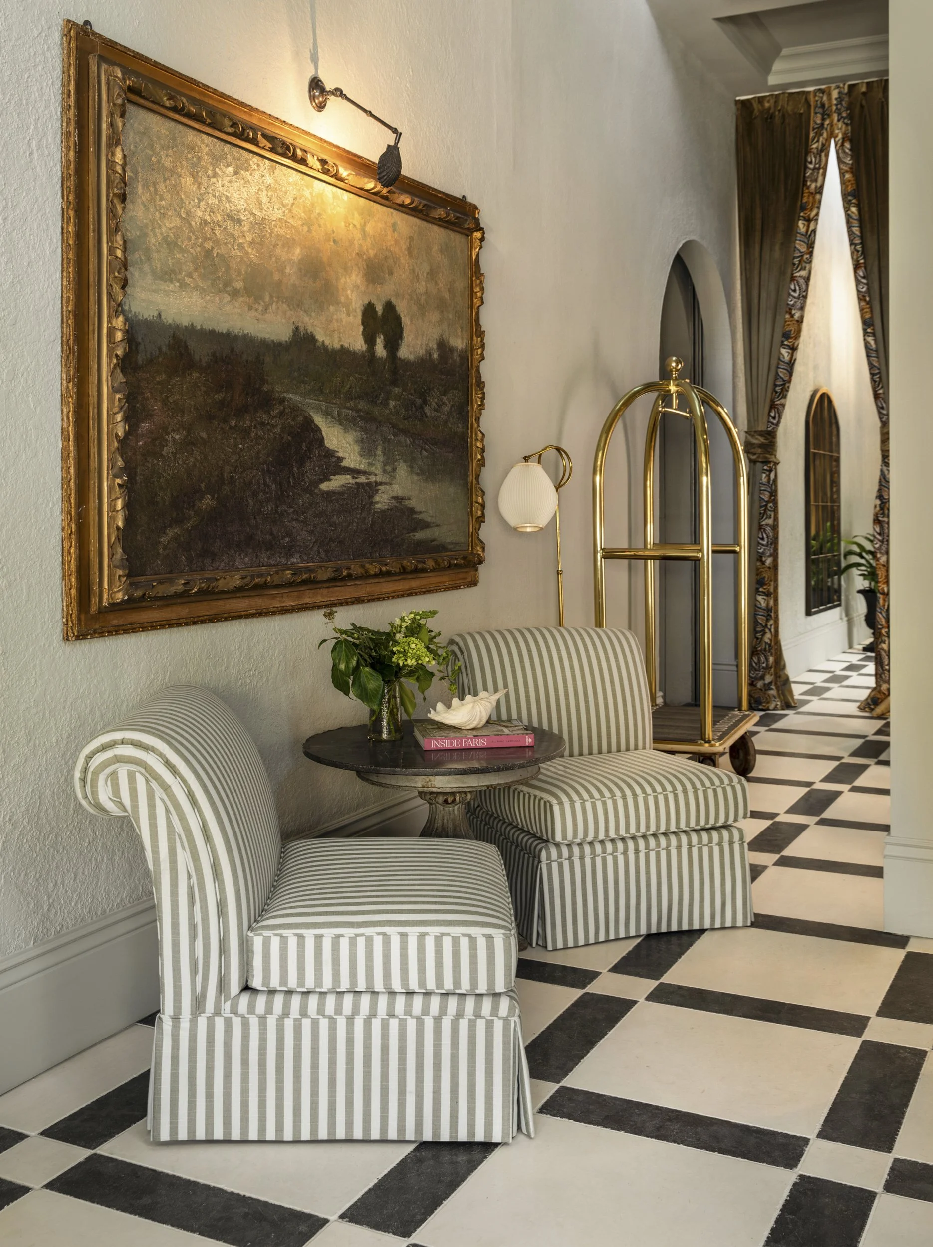 Lobby with gilt-framed landscape painting, striped slipper chairs and checkerboard marble floor at the Perle