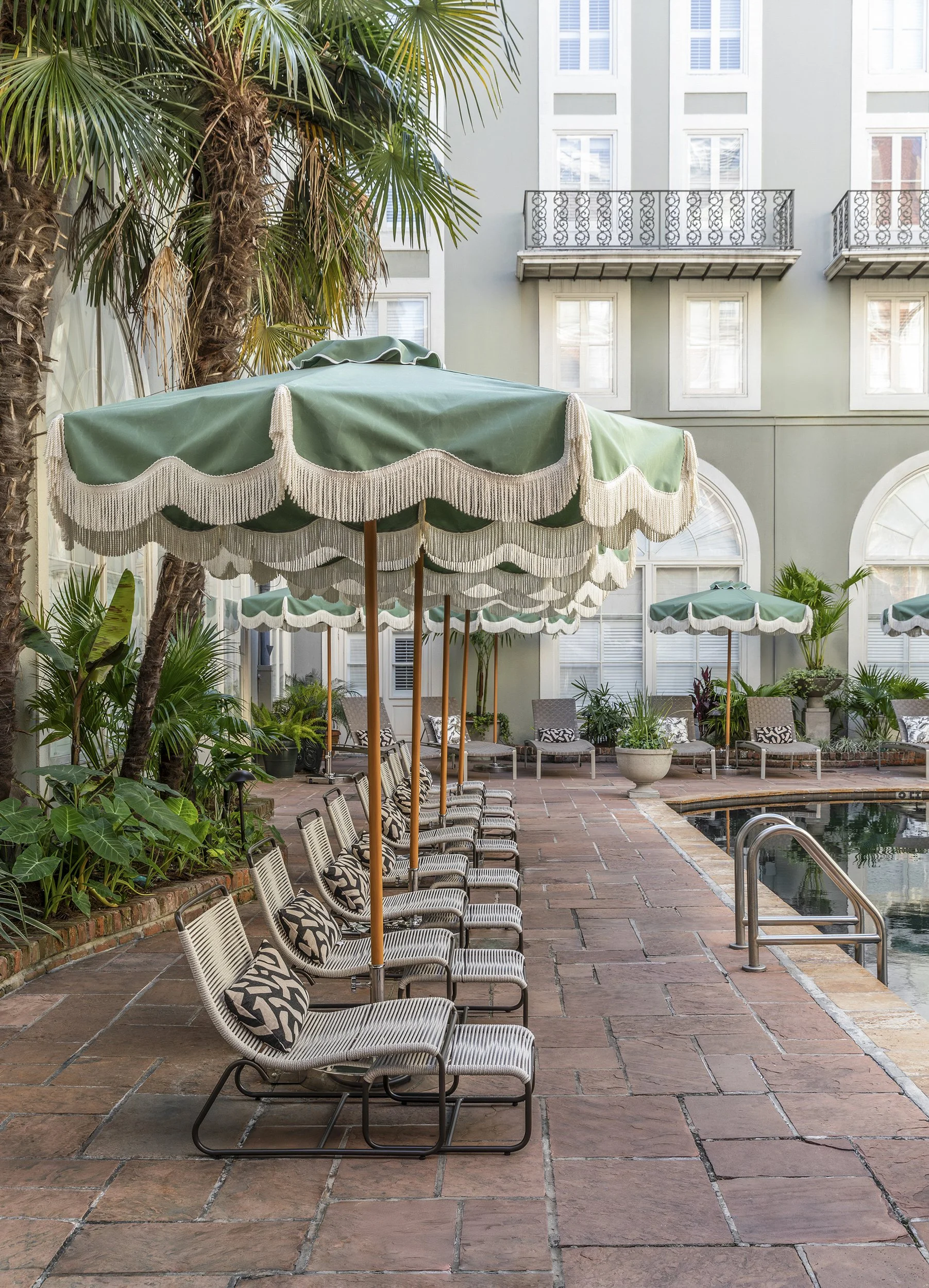 Courtyard pool with green striped umbrellas and lounge chairs at the Bourbon Orleans