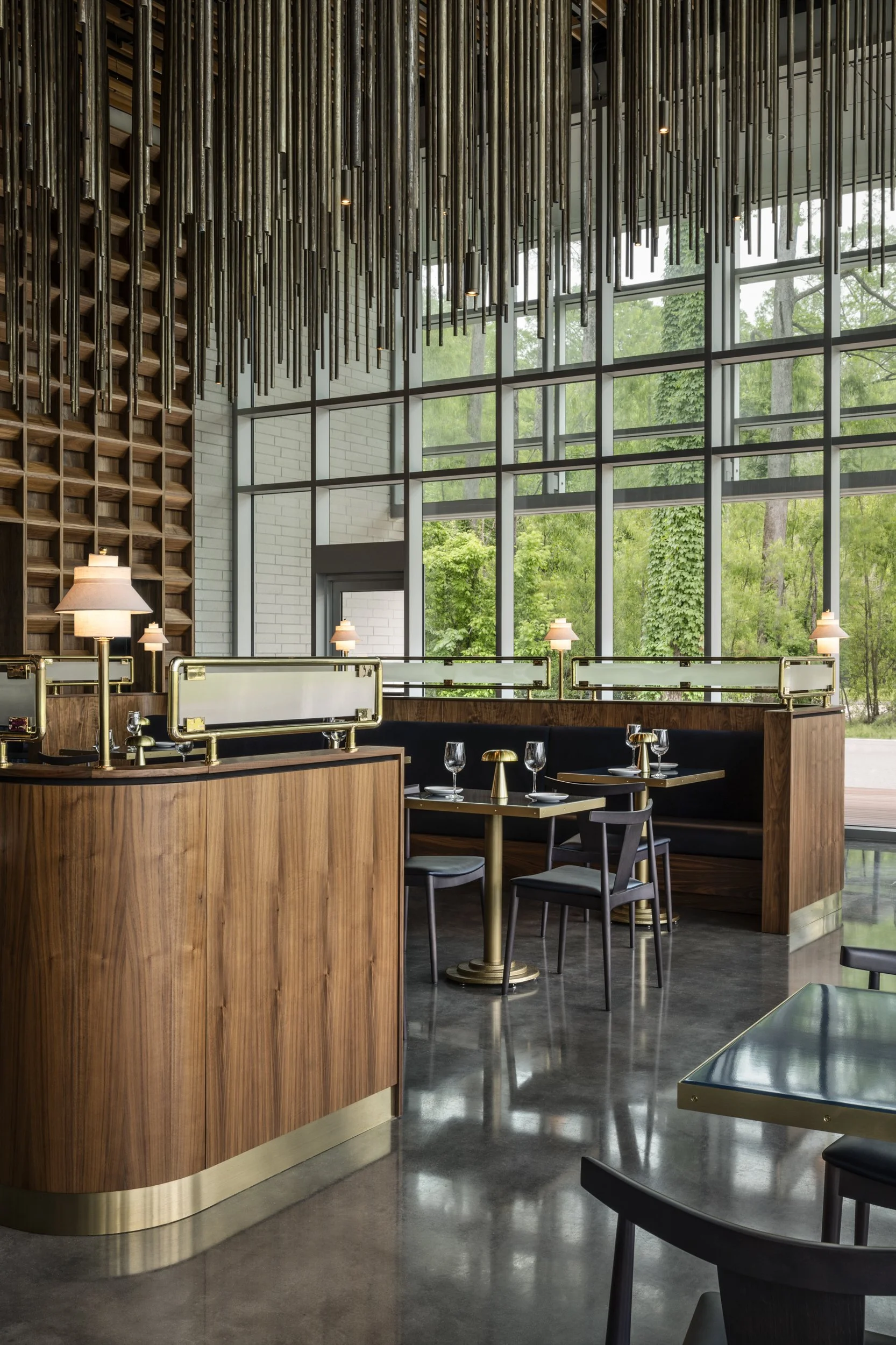 Walnut host stand and brass rails against two-story windows at Tsunami, Baton Rouge