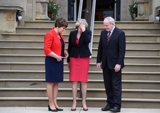 Theresa May facepalming whilst stood between current first minister Arlene Foster and former deputy first minister the late Martin McGuinness last year. Credit: Charles McQuillan/Getty Images