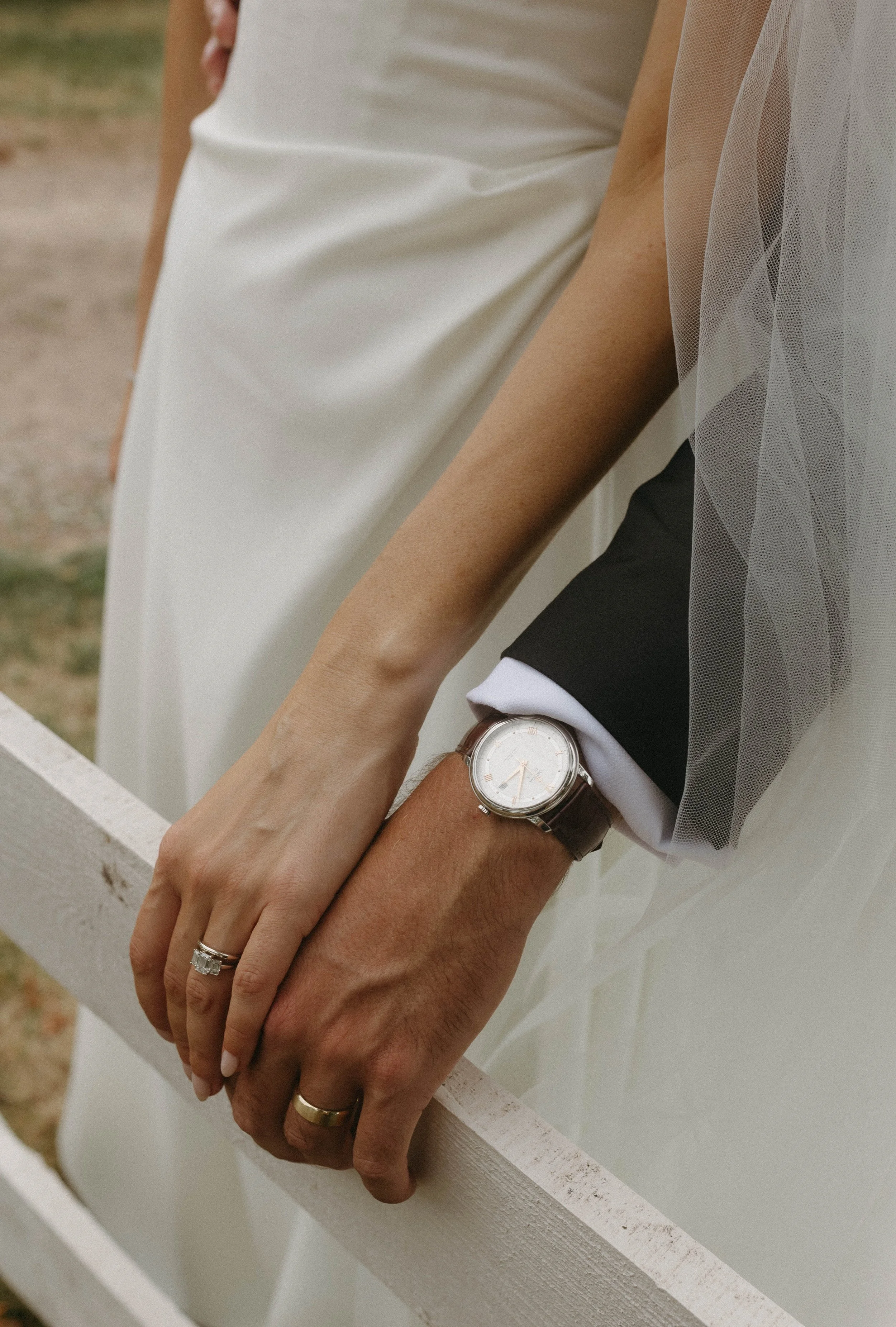 Close-up of a bride and groom holding hands during a wedding, showing rings and a watch on the groom's wrist.